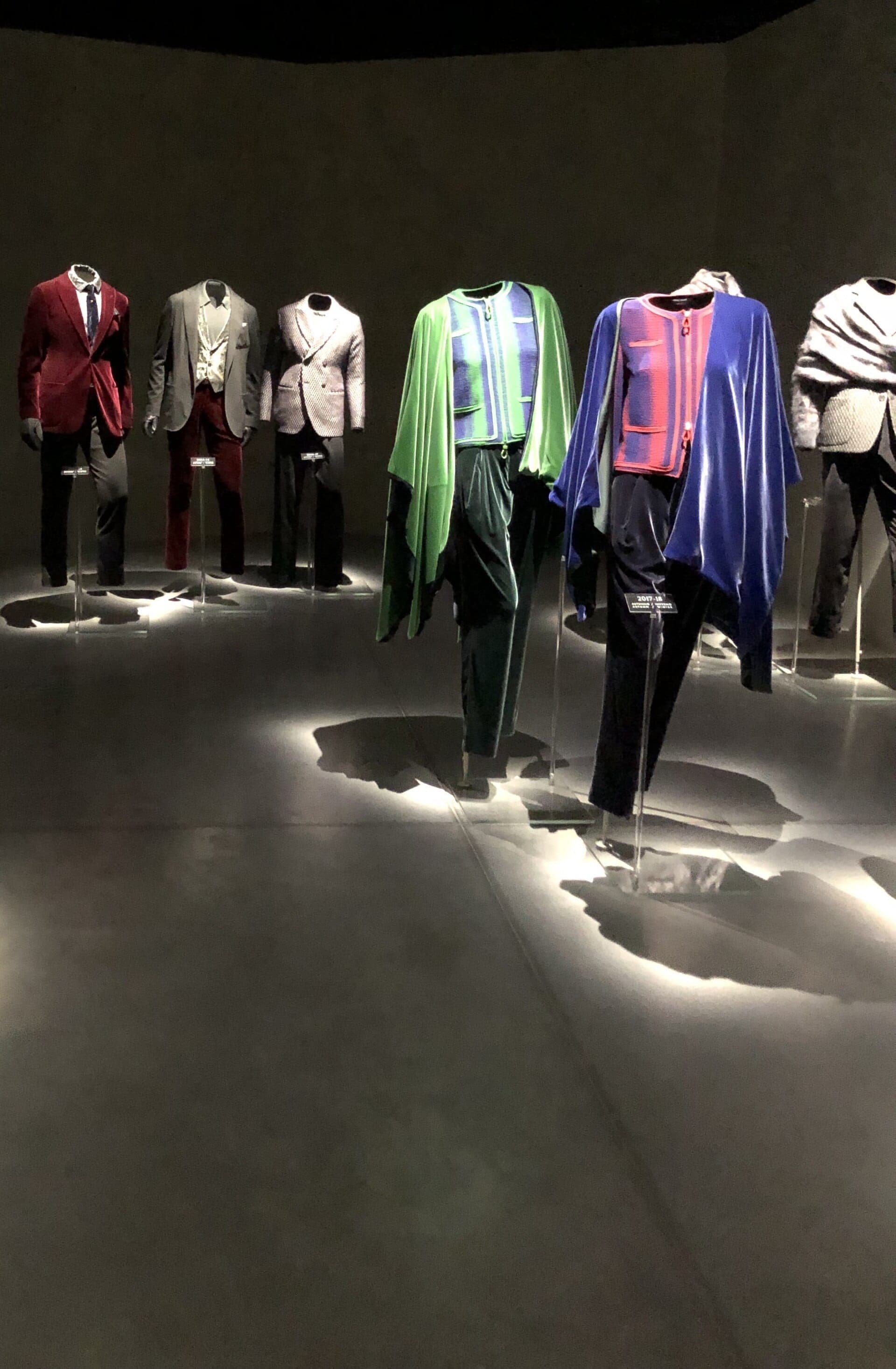 Mannequins displaying Giorgio Armani’s distinctive suits and capes under spotlights inside the dimly lit Armani/Silos fashion museum in Milan.