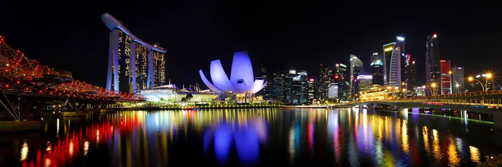 Panoramic night view of Marina Bay with the illuminated ArtScience Museum, Marina Bay Sands, and city skyline reflecting on the water.