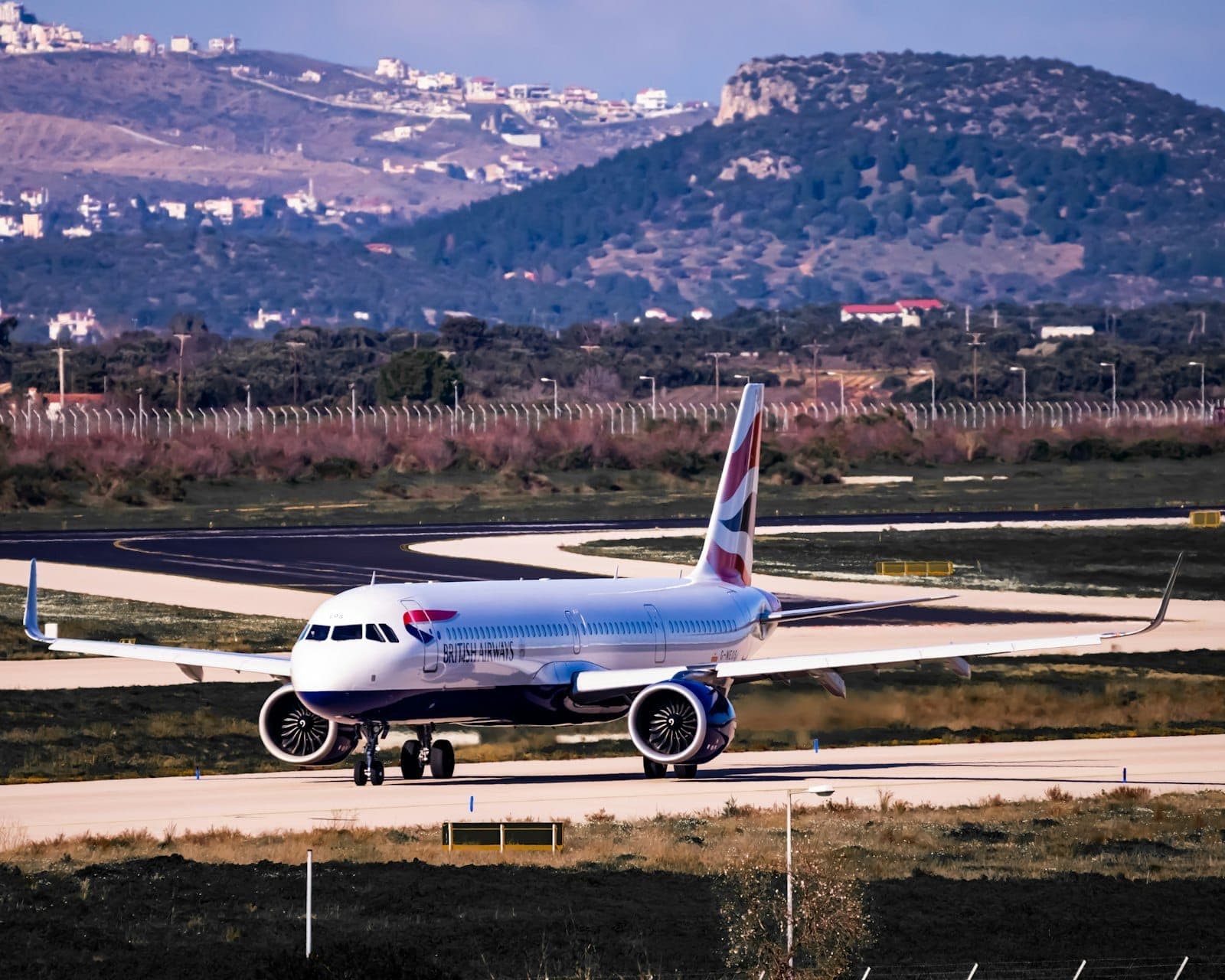 Verkehrsflugzeug rollt auf der Startbahn des Flughafen Athen-Eleftherios Venizelos, mit umliegenden Hügeln und Landschaft im Hintergrund.