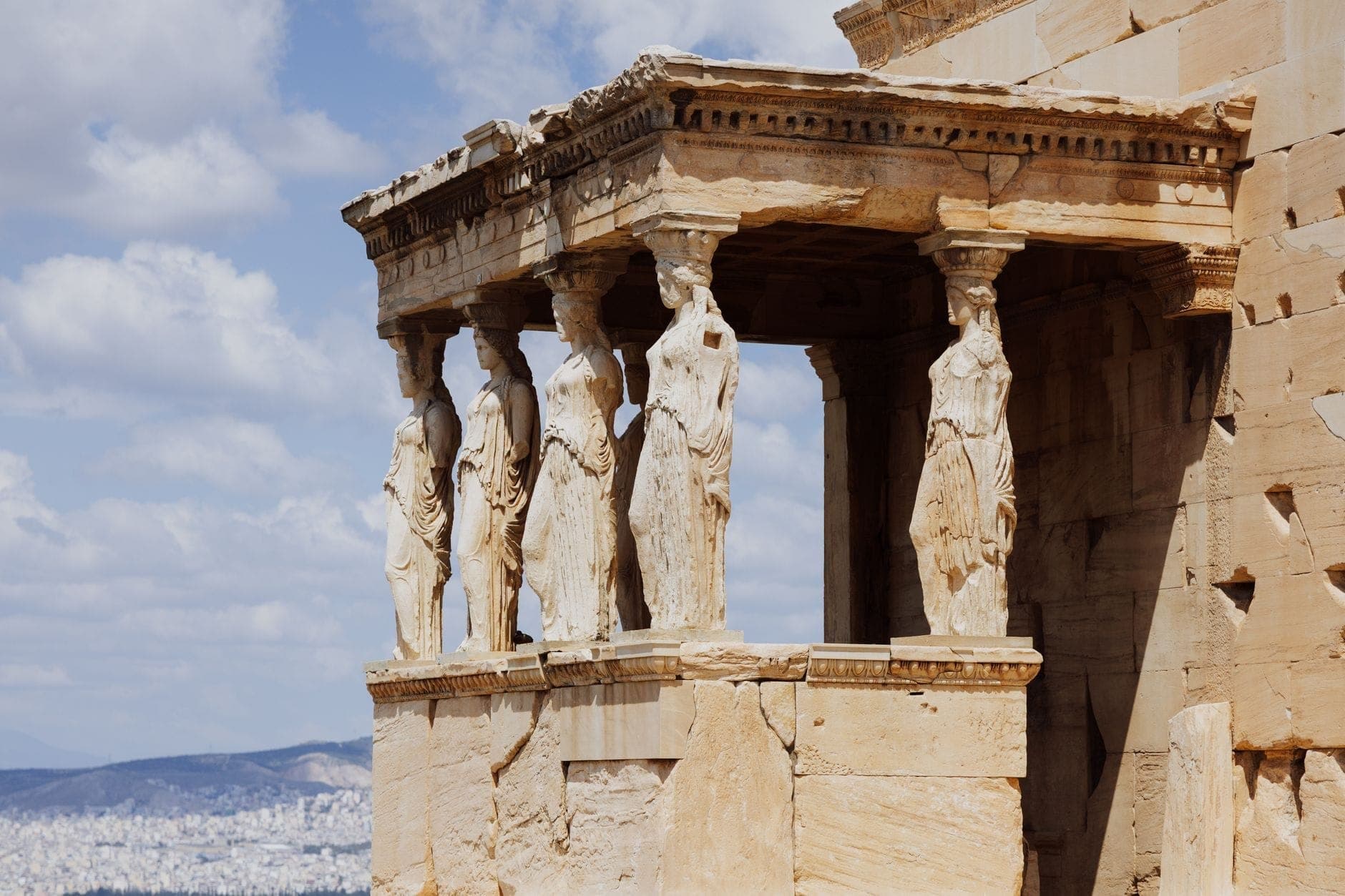 Vista ravvicinata dell'Eretteo con il suo famoso portico delle Cariatidi sull'Acropoli di Atene, paesaggio urbano sullo sfondo.