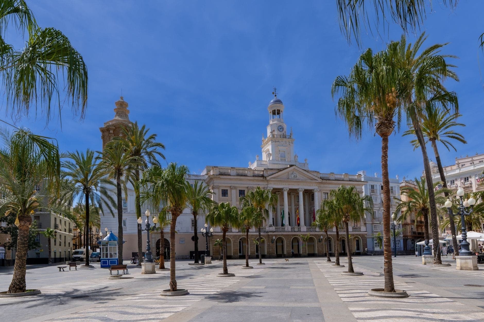 Toàn cảnh góc rộng Ayuntamiento de Cádiz tại quảng trường San Juan de Dios, viền bởi hàng cọ dưới bầu trời xanh sáng, tạo không gian quảng trường thân thiện.
