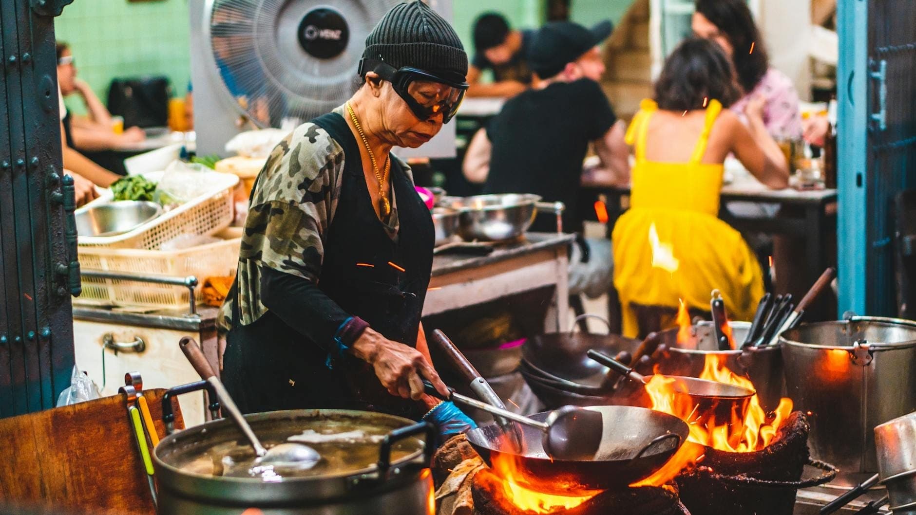 Người bán hàng rong đang xào đồ ăn bằng chảo wok trên lửa lớn tại chợ đêm Bangkok