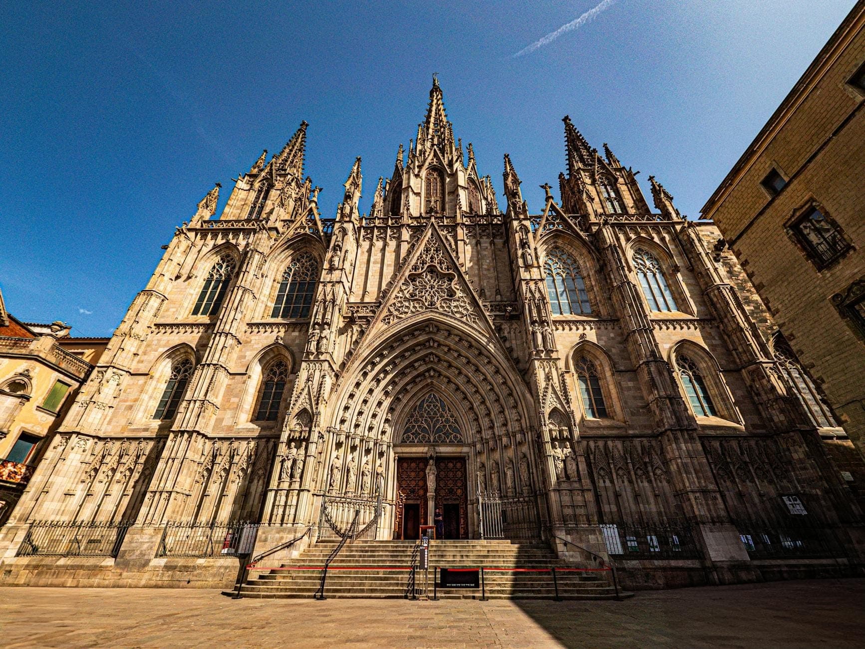 Góc rộng chụp mặt tiền Gothic hoa mỹ của Nhà thờ Barcelona dưới bầu trời xanh trong, với những chi tiết chạm khắc tinh xảo và cổng chính hoành tráng, mời gọi du khách khám phá kiến trúc lịch sử.