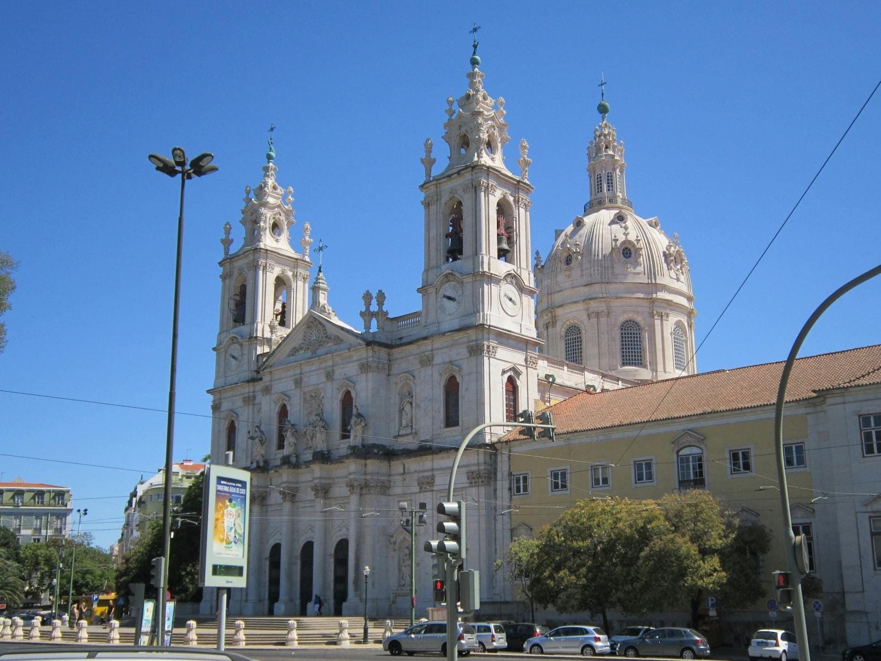 Mặt tiền Basílica da Estrela ở Lisbon dưới bầu trời xanh trong, với hai tháp chuông và mái vòm lớn nổi bật giữa các con phố của thành phố.