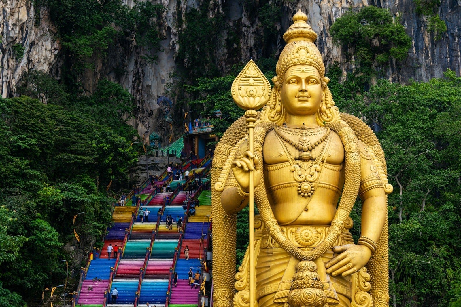 Du khách leo lên những bậc thang cầu vồng mang tính biểu tượng tại Batu Caves dưới bức tượng sừng sững, bắt đầu hành trình đầy màu sắc khám phá quần thể đền thờ Hindu nổi tiếng của Malaysia.
