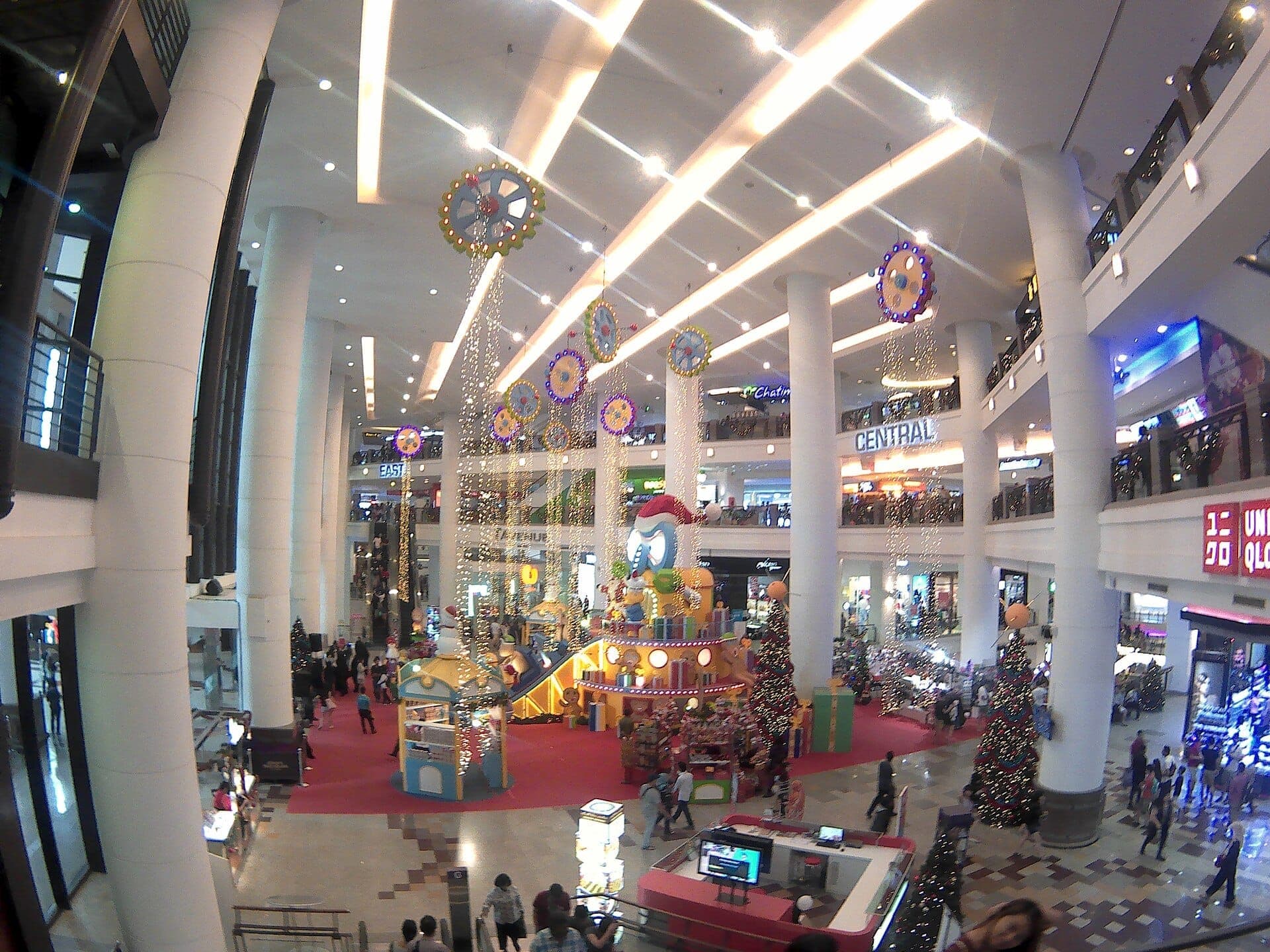 Góc nhìn rộng của sảnh atrium sáng sủa và rộng rãi tại Berjaya Times Square với trang trí lễ hội, những cột trụ cao, nhiều tầng và đông đảo người mua sắm.