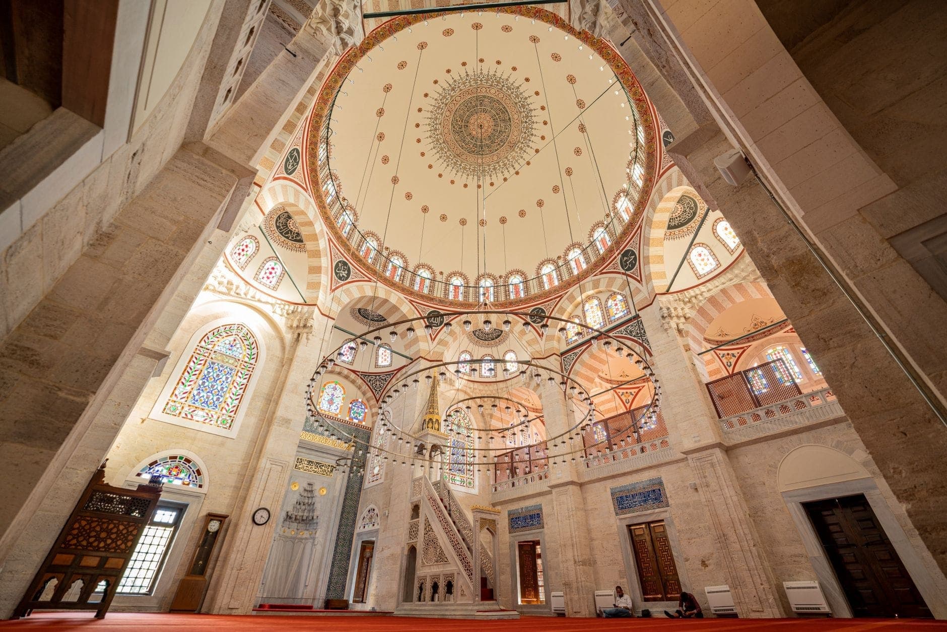 Vista gran angular del interior de una gran mezquita en Estambul con una cúpula ornamentada, vidrieras y detalles arquitectónicos intrincados.