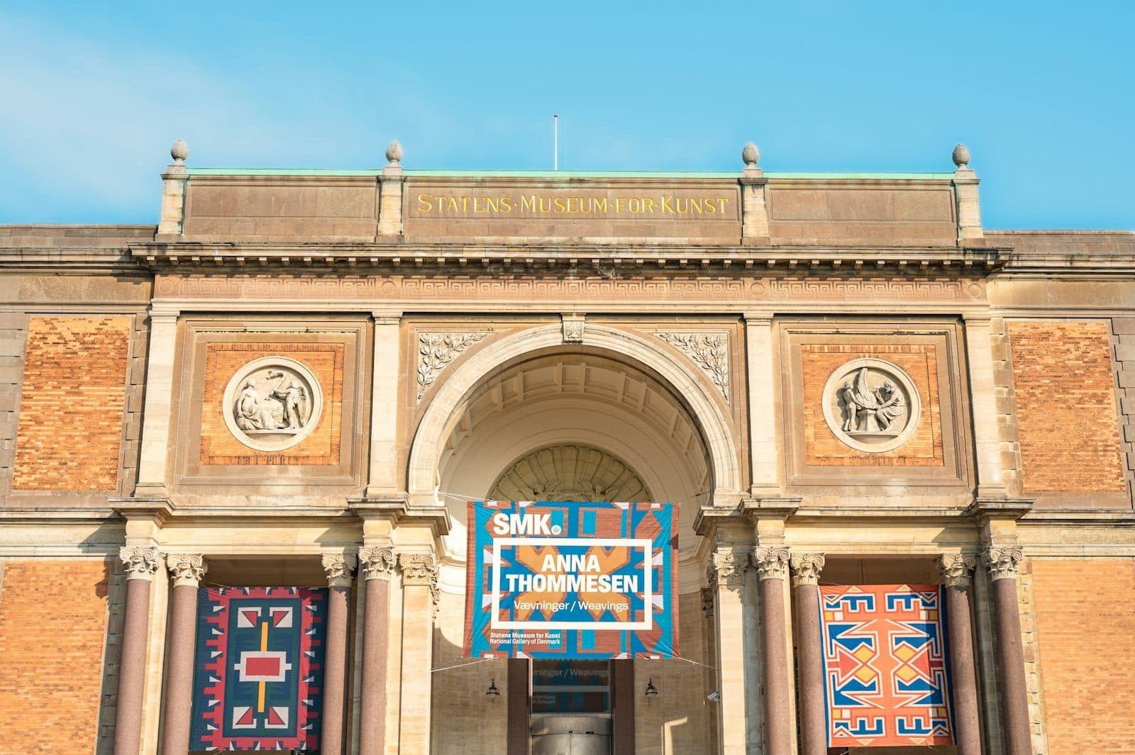 Główne wejście do Statens Museum for Kunst z banerami i klasycznymi detalami architektonicznymi pod błękitnym niebem