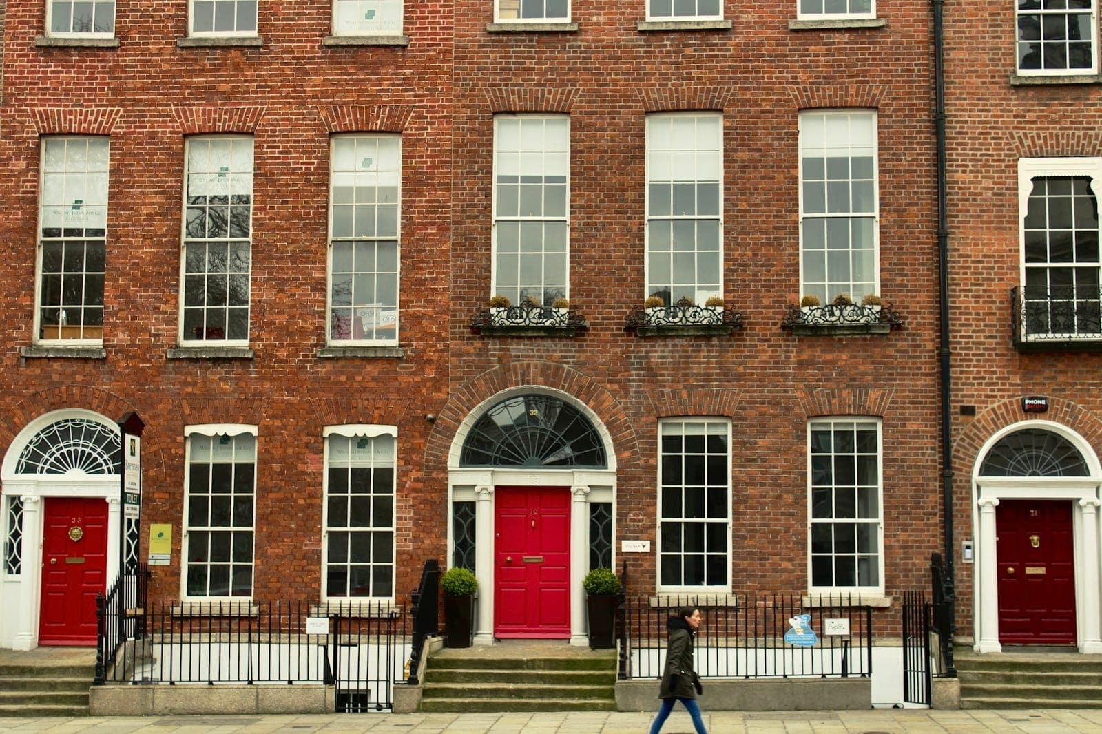 Historyczny georgiański budynek z cegły z wysokimi oknami skrzydłowymi i kolorowymi drzwiami na ulicy Dublina, oddający klasyczną irlandzką architekturę.