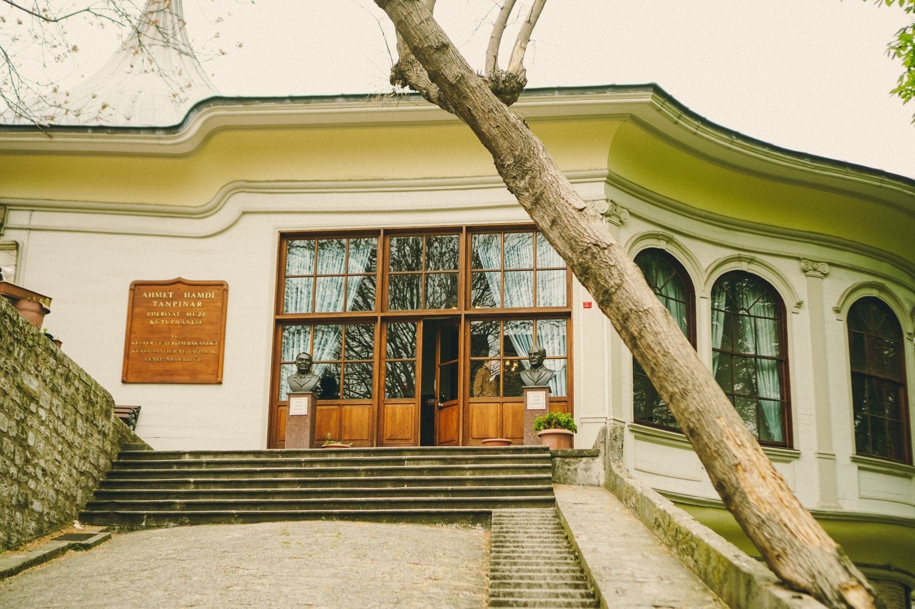 Fachada de un museo único en Estambul con una placa, escalones, ventanas arqueadas y un árbol inclinado al frente.