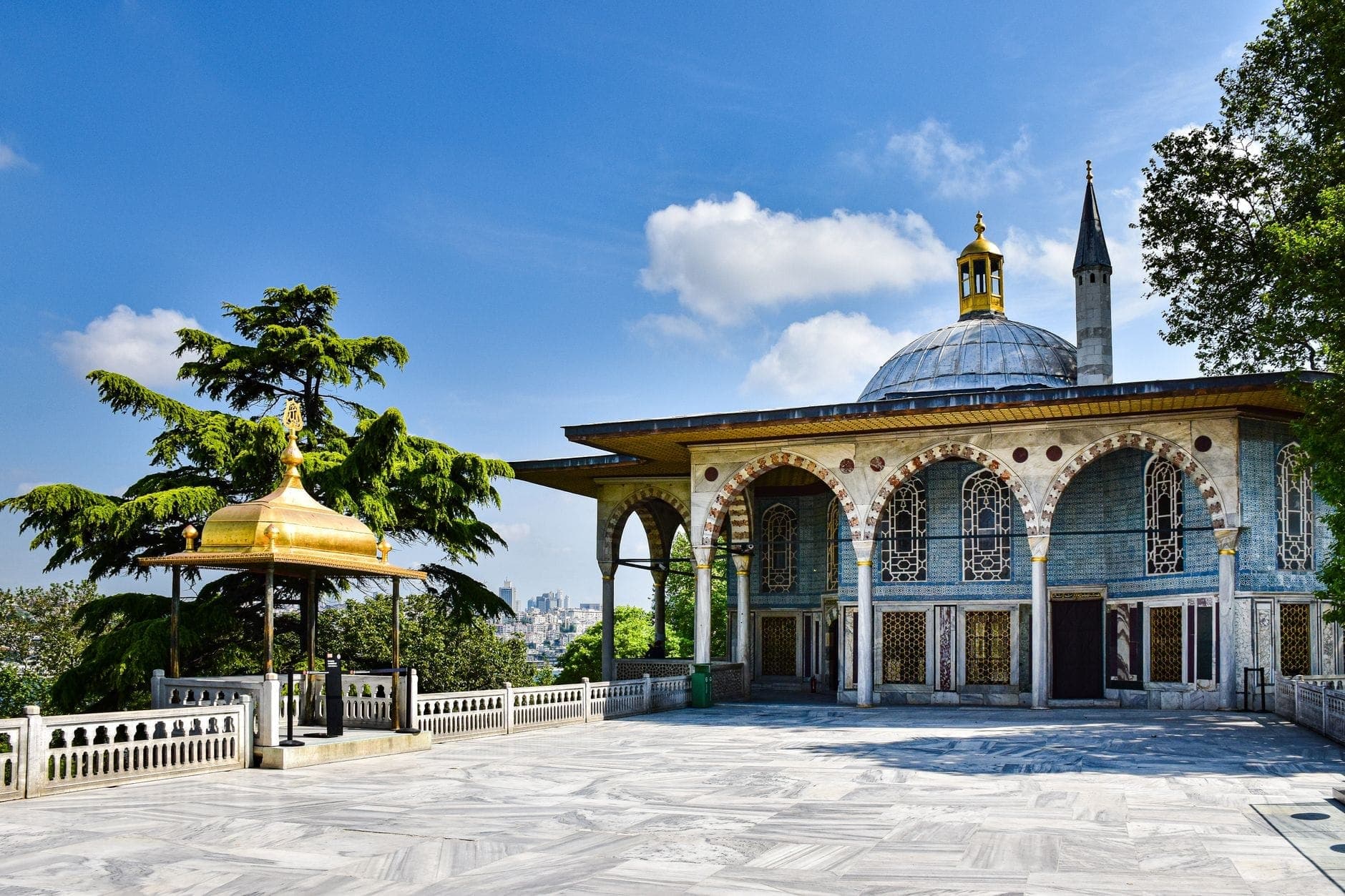 Una impresionante vista del Palacio de Topkapı en Estambul bajo un cielo azul brillante, mostrando su ornamentado pabellón con cúpula y su elegante terraza de mármol.