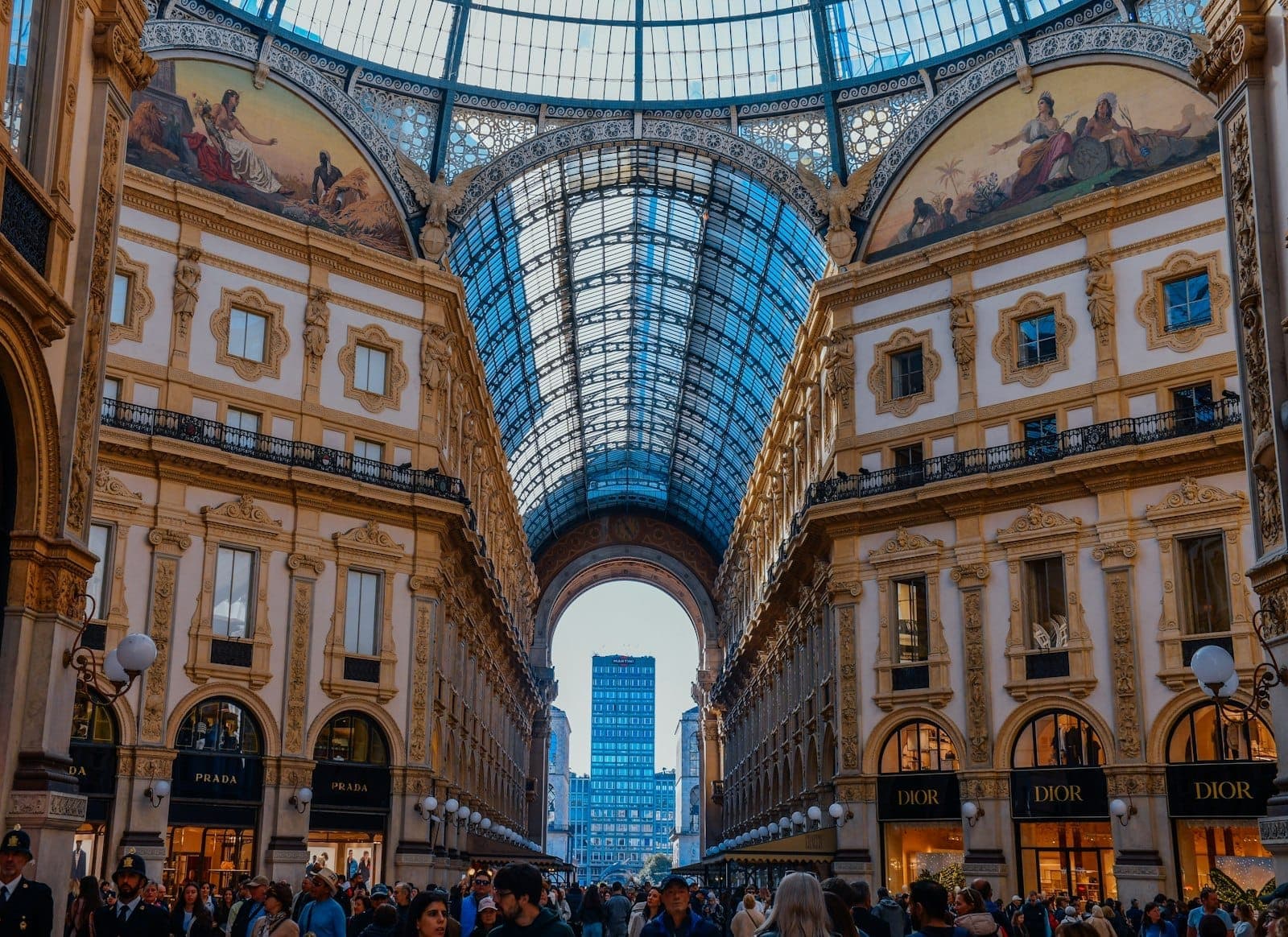 Элегантная Galleria Vittorio Emanuele II в Милане со стеклянной крышей, толпы людей, прогуливающихся мимо дизайнерских магазинов и богато украшенной архитектуры.