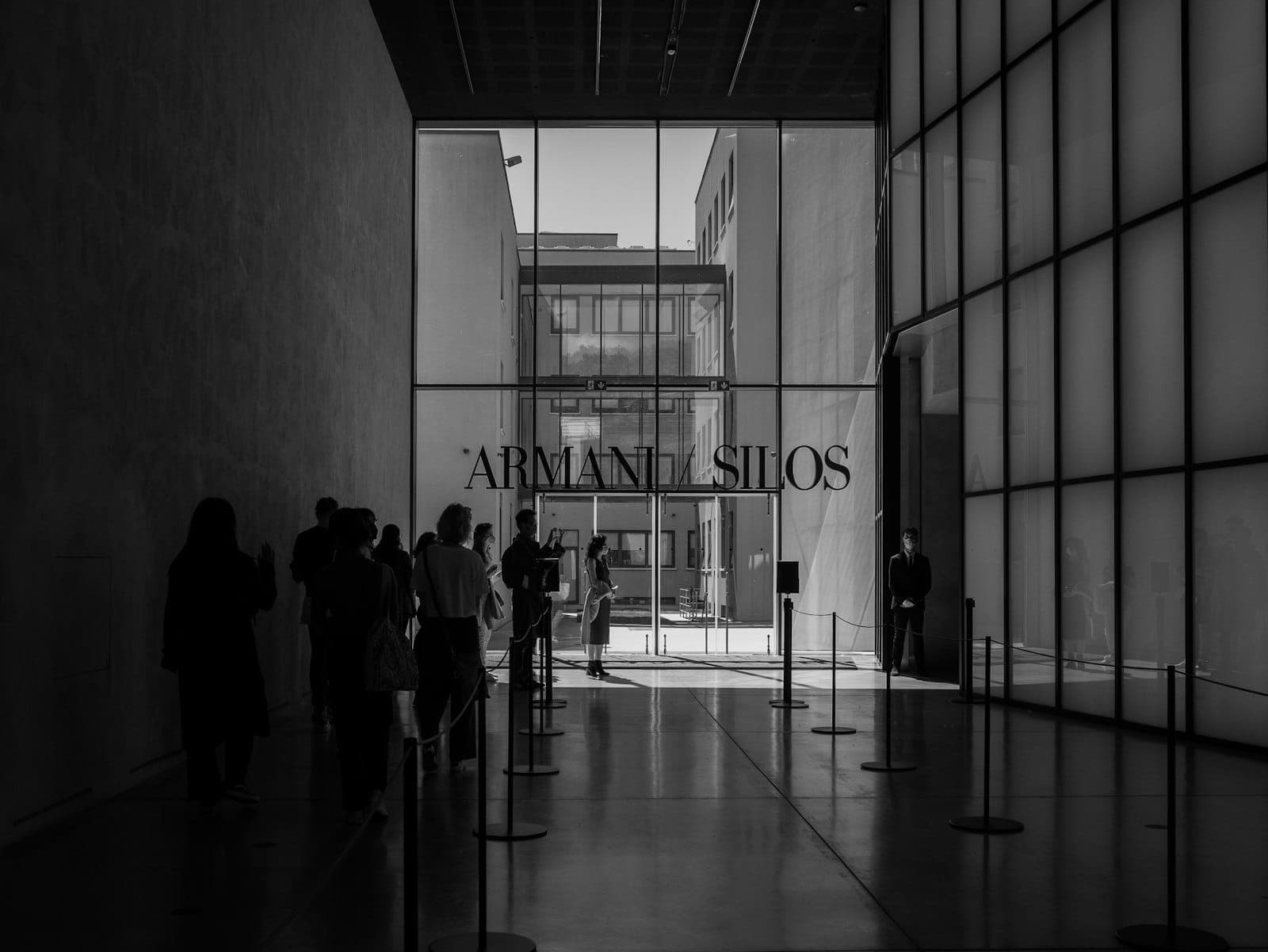 Современный стеклянный входной холл музея Armani Silos в Милане с людьми, стоящими и ходящими внутри.