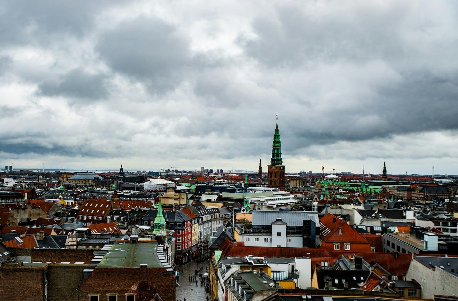 Overcast skies above Copenhagen’s cityscape with brick rooftops and church spires, illustrating the city’s typical cloudy, temperate climate.