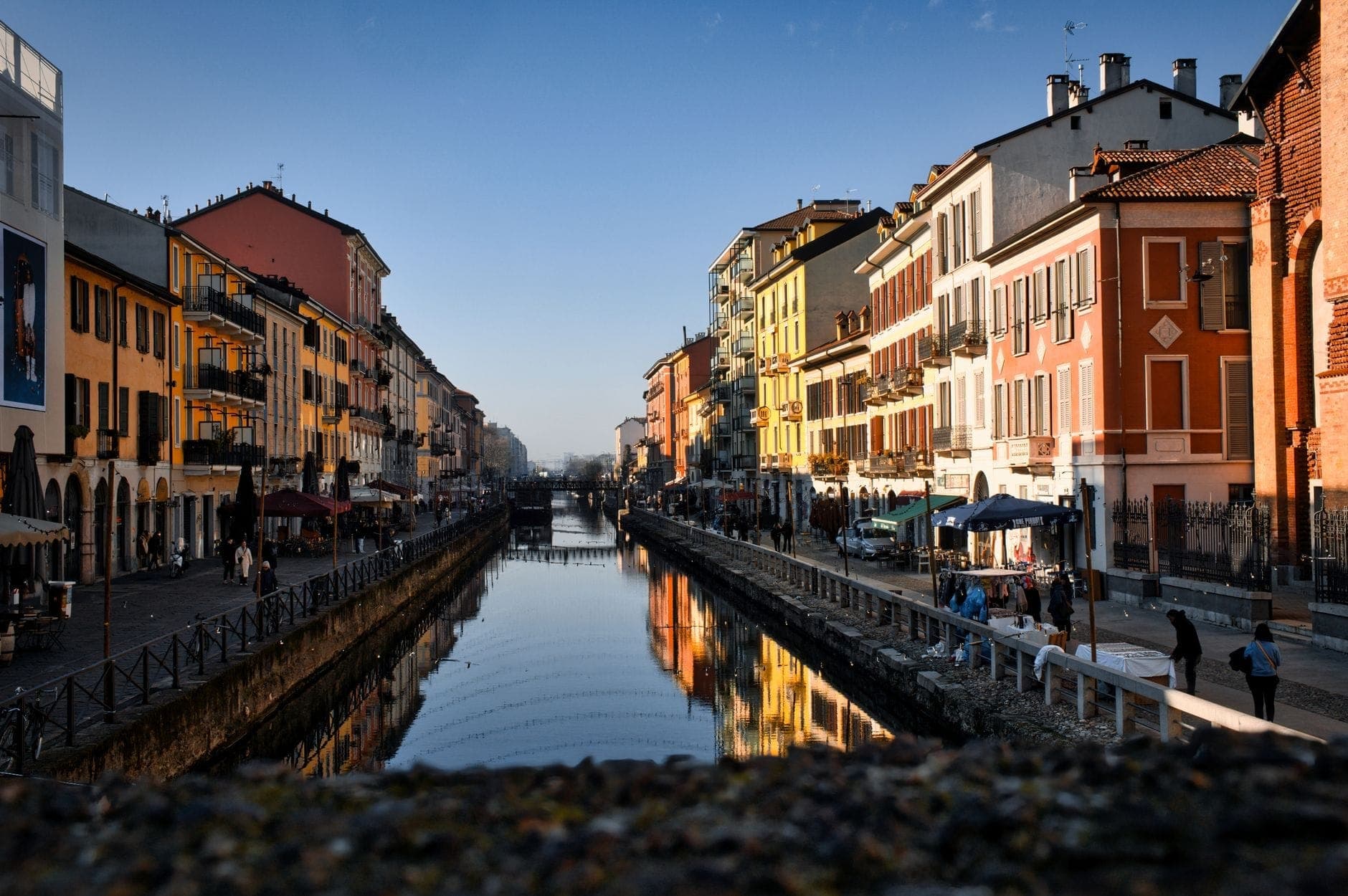 Blick auf den Navigli-Kanal in Mailand, gesäumt von bunten Gebäuden und Menschen, die an einem sonnigen Herbsttag spazieren gehen.