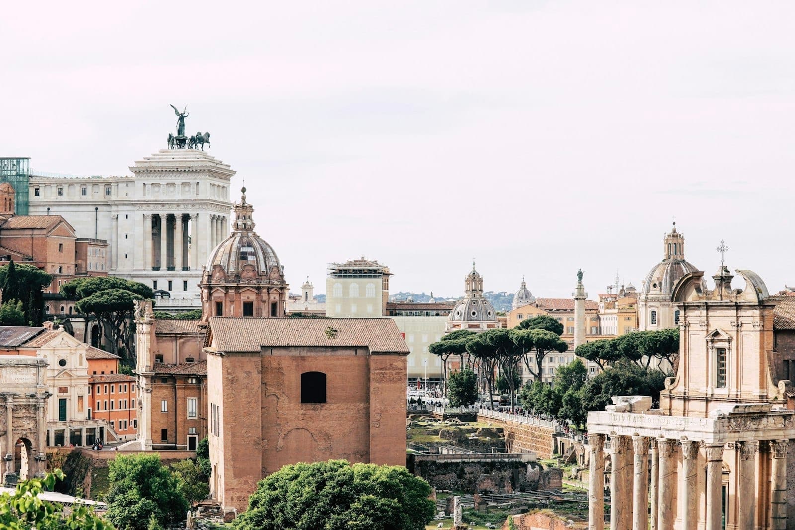 Toàn cảnh thành Rome với những mái vòm lịch sử, phế tích cổ đại và cây xanh tươi tốt dưới bầu trời trong sáng.