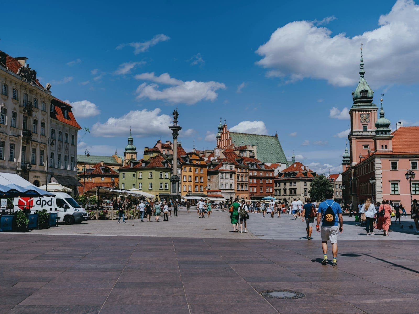Ein lebhafter Blick auf den Warschauer Altmarkt an einem sonnigen Tag mit bunten historischen Häusern, flanierenden Menschen und strahlend blauem Himmel.