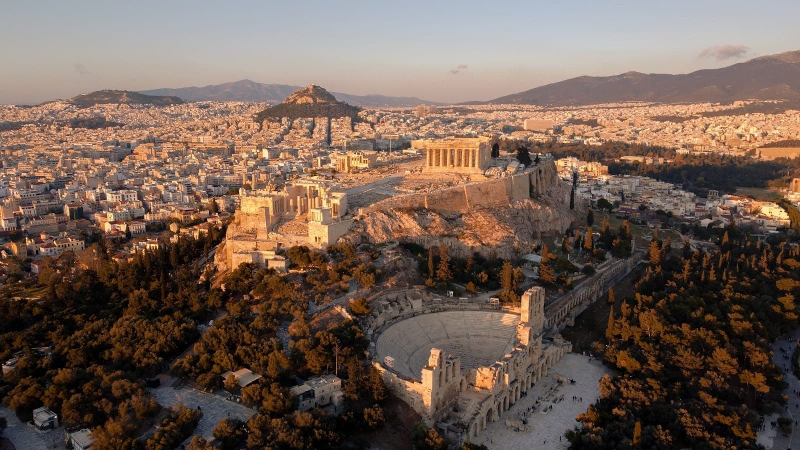 Vista aerea dell'Acropoli e dei suoi pendii ad Atene, con il Partenone e l'Odeon di Erode Attico visibili, circondati dal paesaggio urbano.