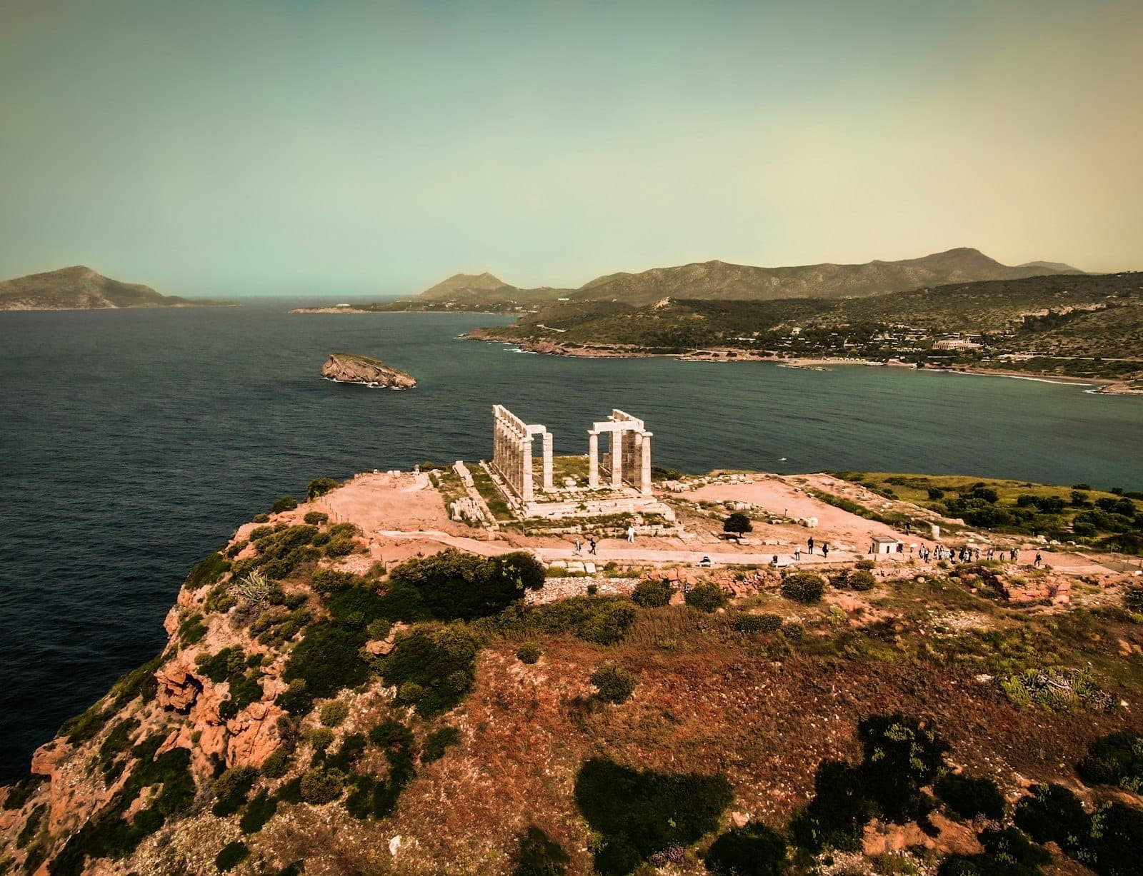 Vista aerea del Tempio di Poseidone a Capo Sounion su una spettacolare scogliera che domina il mare con le montagne sullo sfondo.