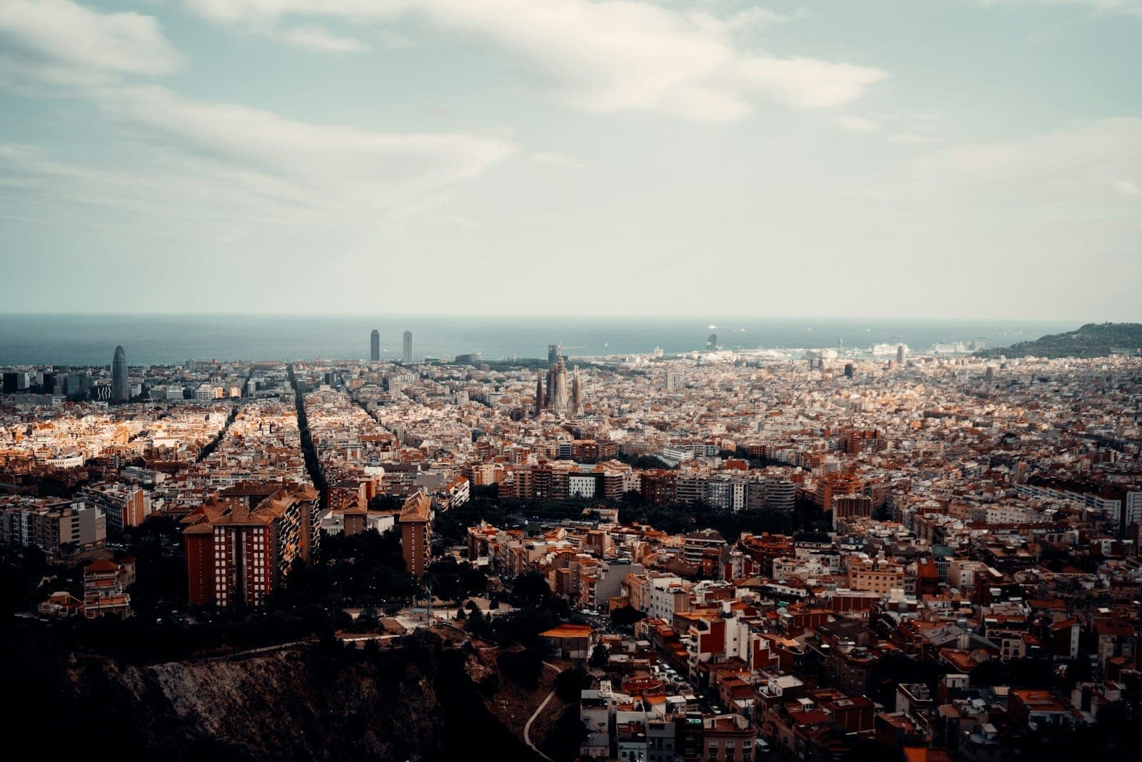 Toàn cảnh Barcelona nhìn từ trên cao với đường chân trời thành phố, tháp Sagrada Família nổi bật và biển Địa Trung Hải dưới bầu trời ấn tượng.
