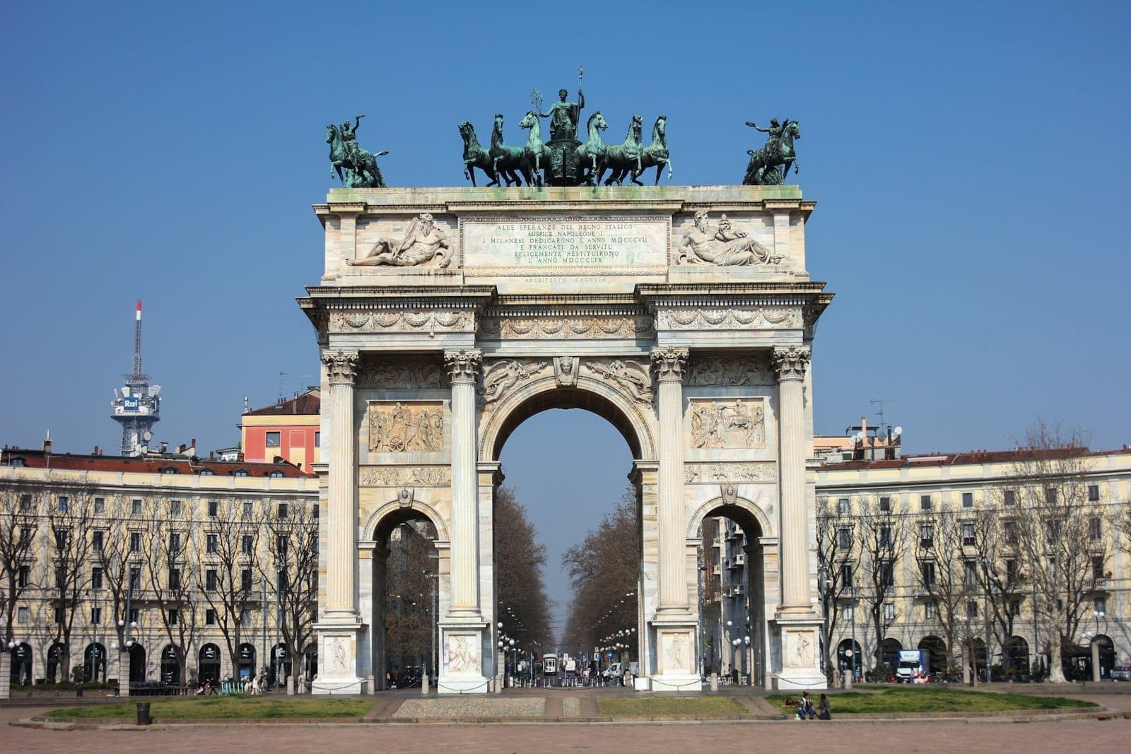 Arco della Pace a Milano visto da un'ampia piazza aperta con linee di visuale chiare e edifici circostanti sotto un cielo azzurro