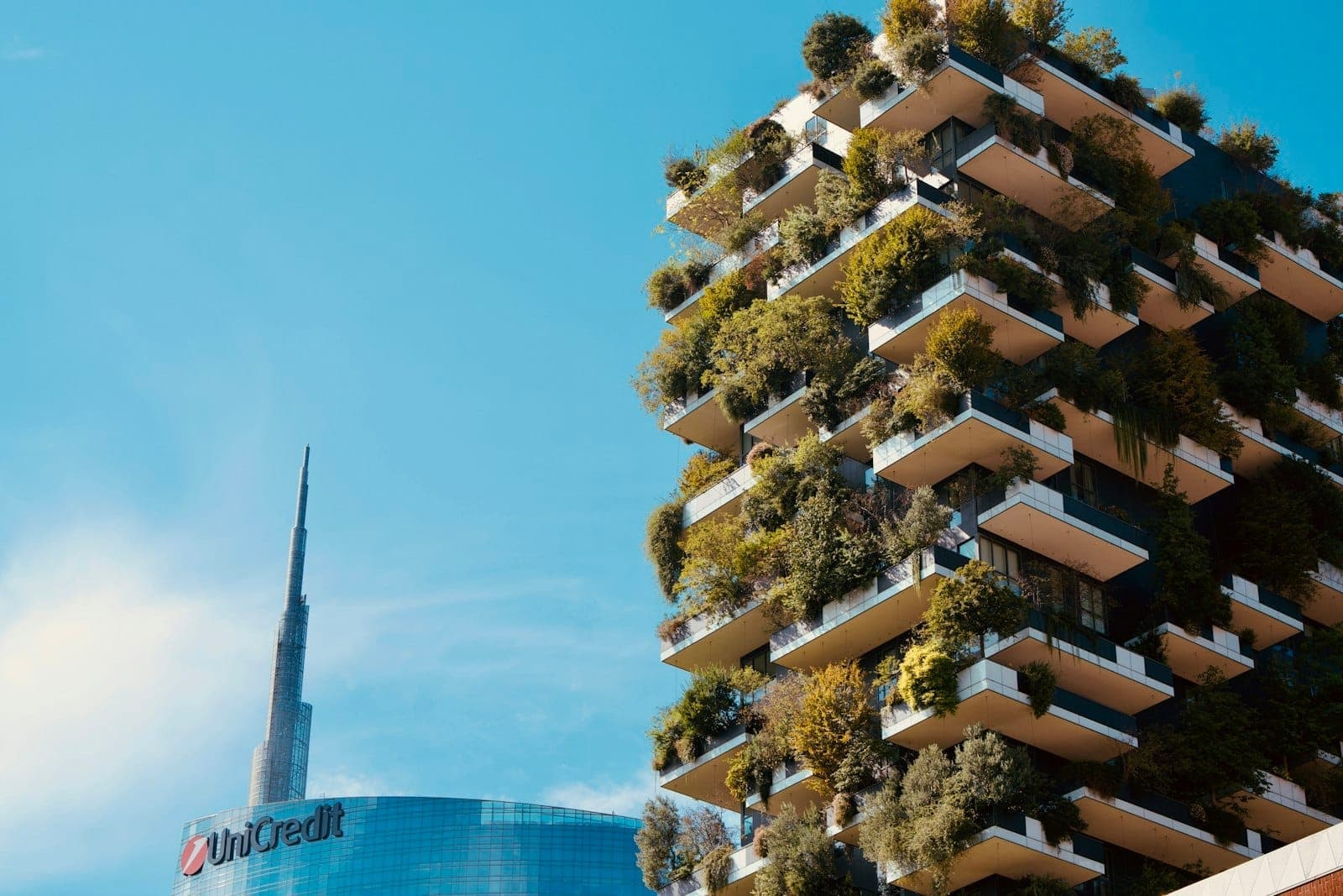 La torre Bosco Verticale e il moderno grattacielo UniCredit fianco a fianco sotto un cielo azzurro nell'innovativo quartiere Porta Nuova di Milano.