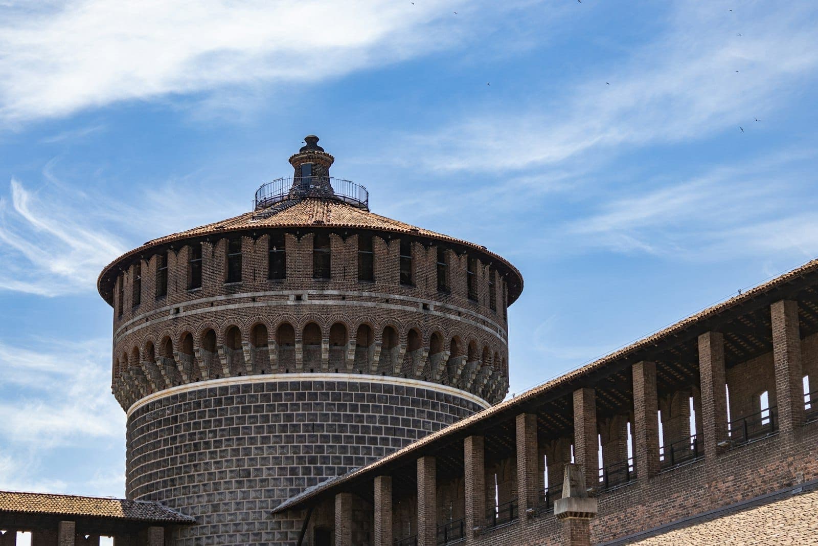 Vista ravvicinata della Torre del Filarete al Castello Sforzesco di Milano sotto un cielo azzurro brillante con nuvole leggere.
