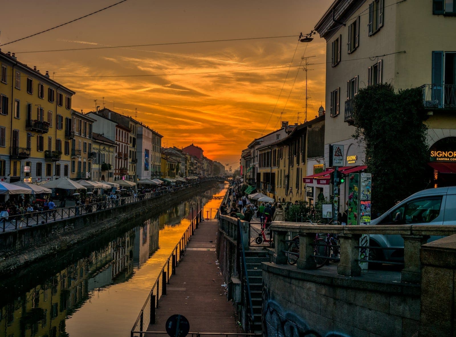 Tramonto sul canale Naviglio Grande a Milano con riflessi, caffè ed edifici colorati lungo l'acqua.