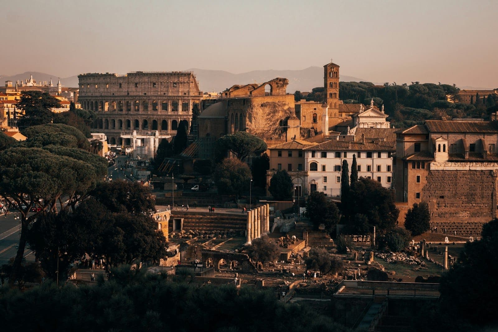 Toàn cảnh Rome lúc hoàng hôn với đấu trường Colosseum và Quảng trường La Mã, những tòa nhà cổ kính và hàng thông dưới ánh sáng vàng ấm áp.