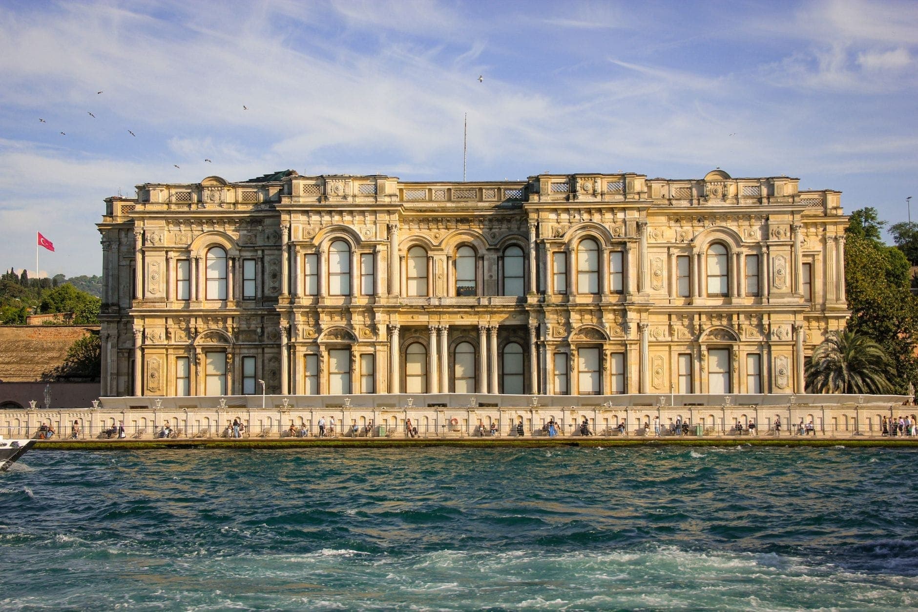 Der Beylerbeyi-Palast vom gegenüberliegenden Bosphorusufer aus, mit seiner prachtvollen neoklassizistischen Fassade, blauem Wasser im Vordergrund und üppigem Grün im Hintergrund unter strahlend blauem Himmel.