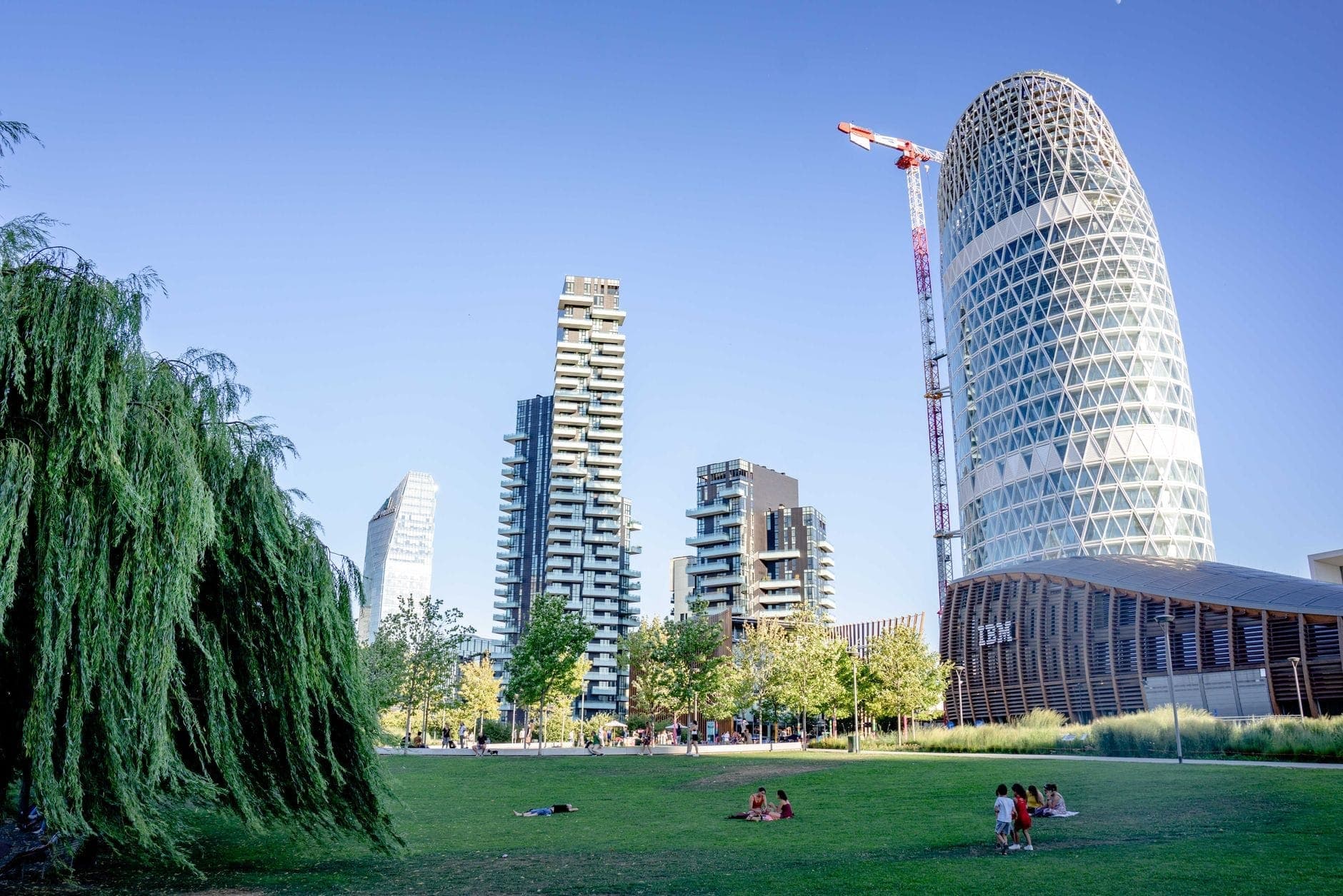Lush green park framed by modern skyscrapers and people relaxing on the grass, representing the contemporary Biblioteca degli Alberi Milano in the Porta Nuova district.