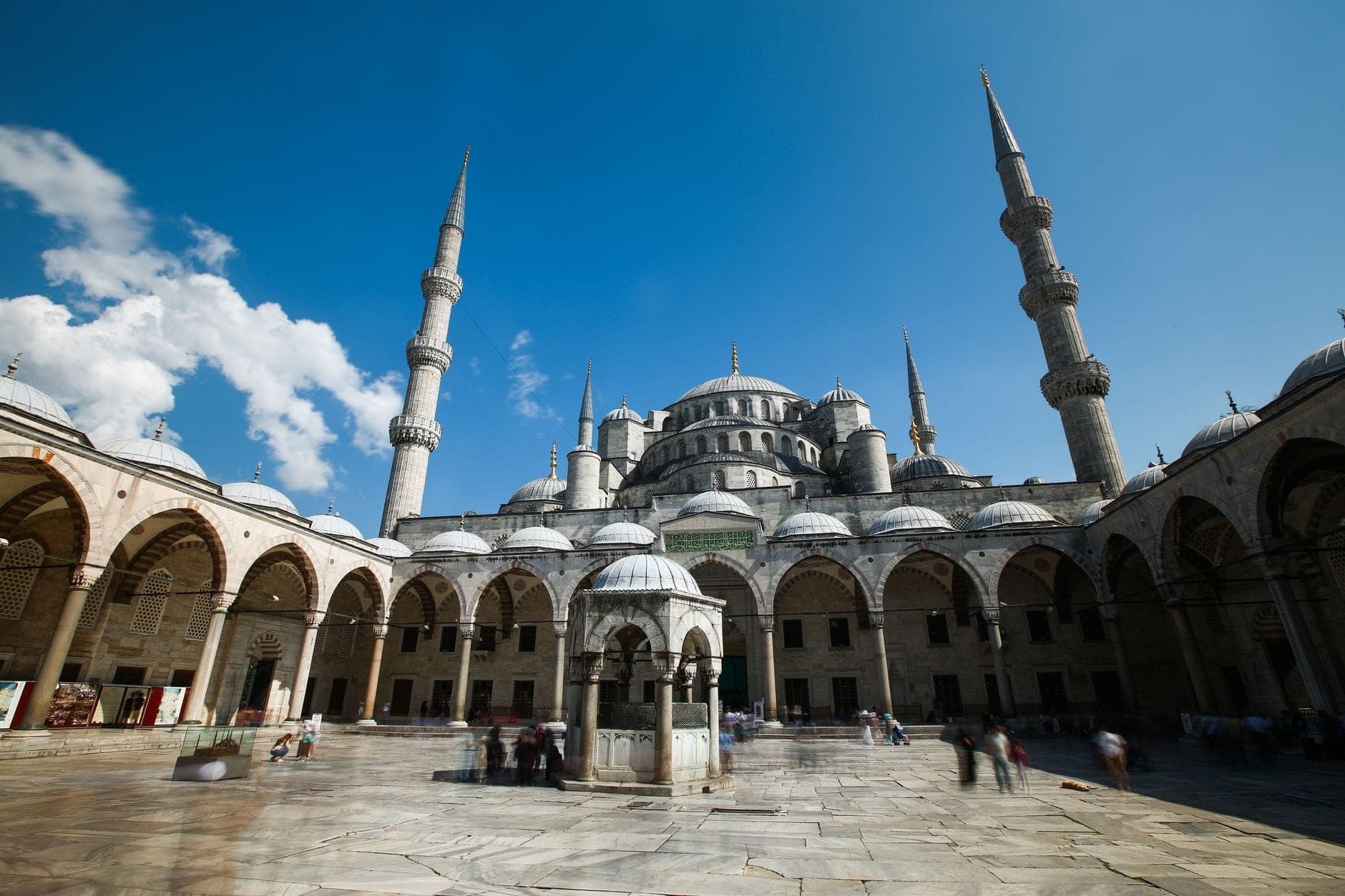 Weitwinkelaufnahme des Innenhofs der Blauen Moschee mit Hauptkuppeln unter strahlend blauem Himmel – die Pracht des Bauwerks und der einladende Eingang kommen voll zur Geltung.
