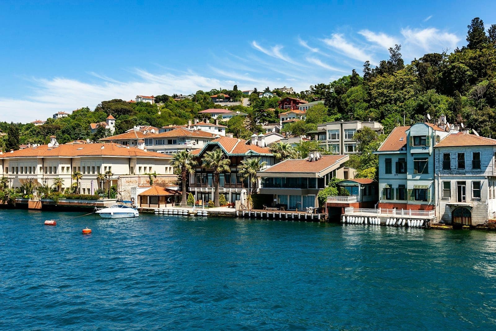 Malerische Bosporus-Uferpromenade mit bunten historischen Villen und üppigem Grün vor blauem Wasser und klarem Himmel in Istanbul.