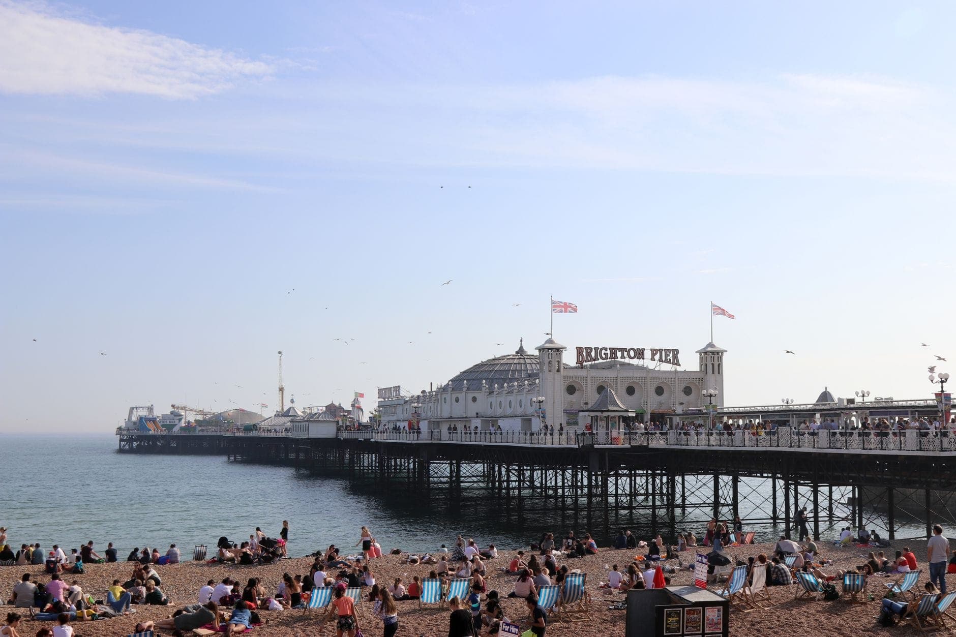 Cầu Brighton trải dài ra biển, du khách thư giãn trên bãi sỏi nhộn nhịp dưới bầu trời xanh trong.