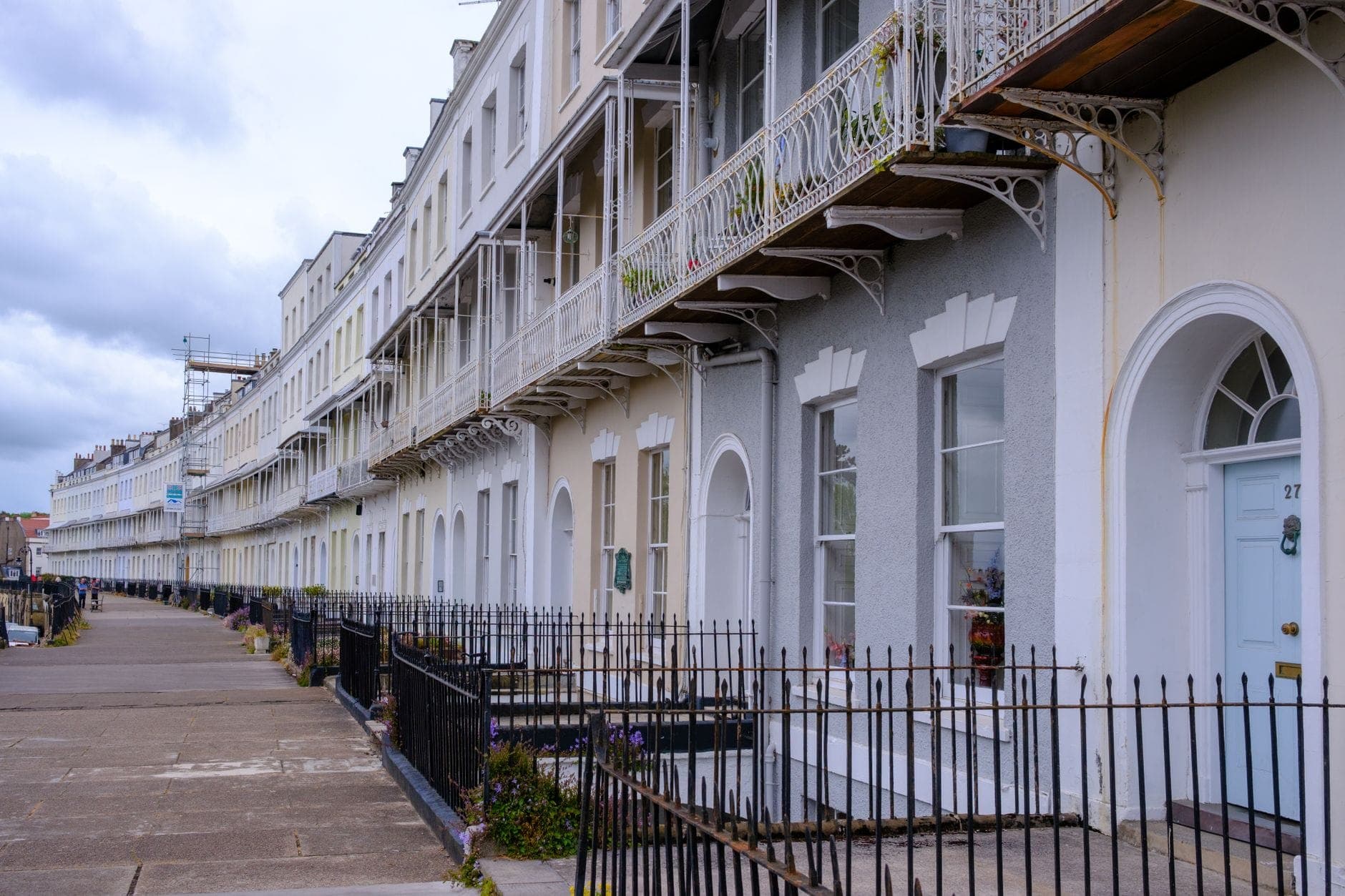 Dãy nhà Regency màu trắng nổi bật ở Brighton với ban công sắt uốn và cửa vòm dưới bầu trời nhiều mây.