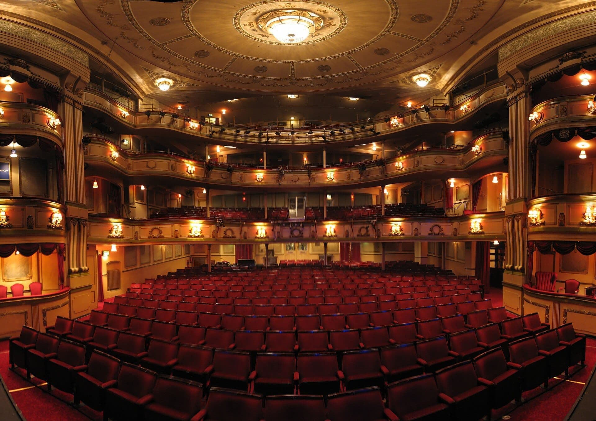 Cảnh nhìn vào khán phòng phong cách Regency được trang trí tinh xảo của Theatre Royal Brighton với ghế nhung đỏ, các tầng ban công và đèn chùm thanh lịch dưới ánh đèn ấm áp.