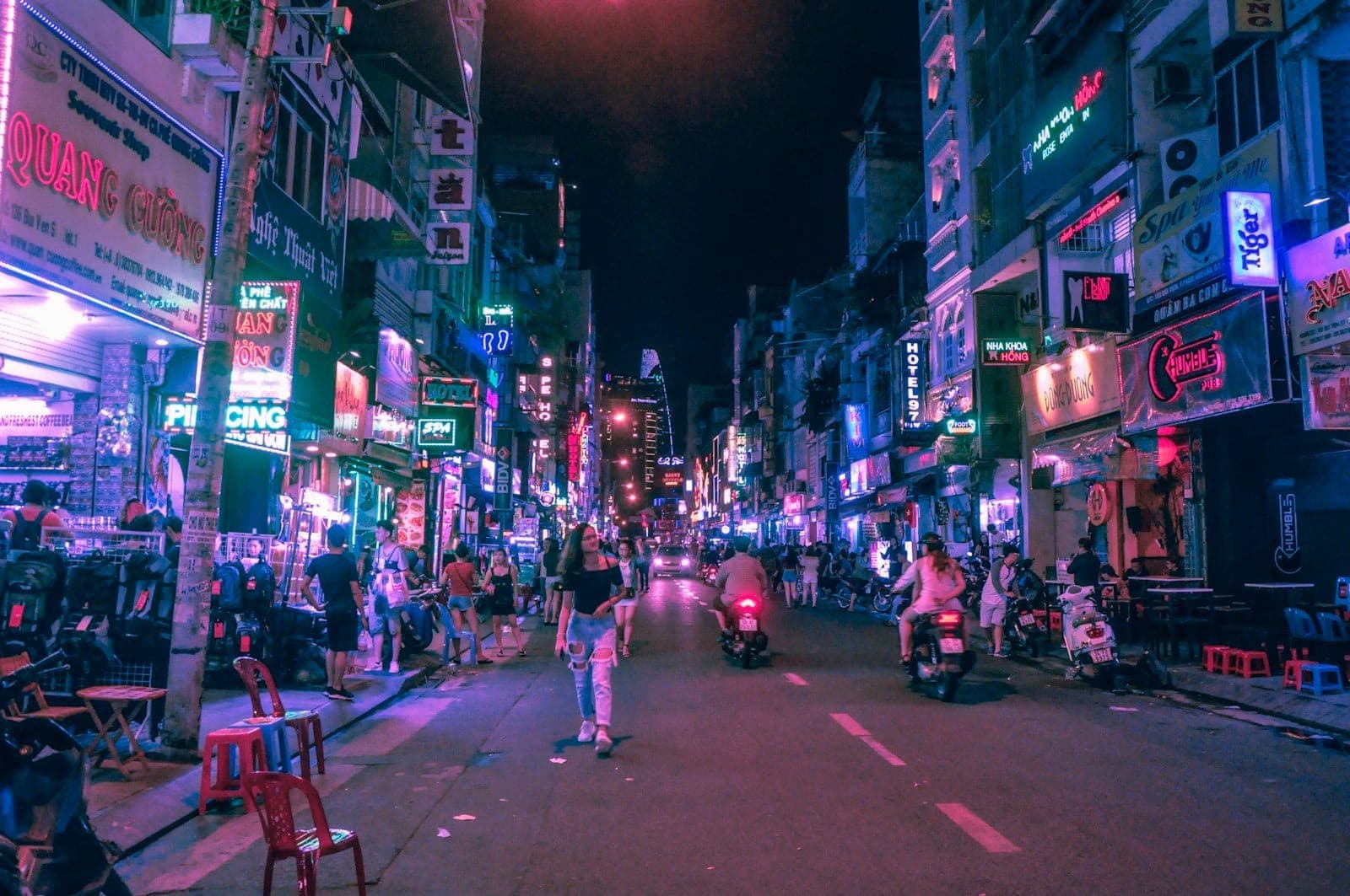 Phố đi bộ Bui Vien về đêm, tấp nập với các quán bar đèn neon, cửa hàng, người đi bộ và xe máy dưới những biển hiệu rực rỡ, đầy màu sắc của thành phố.