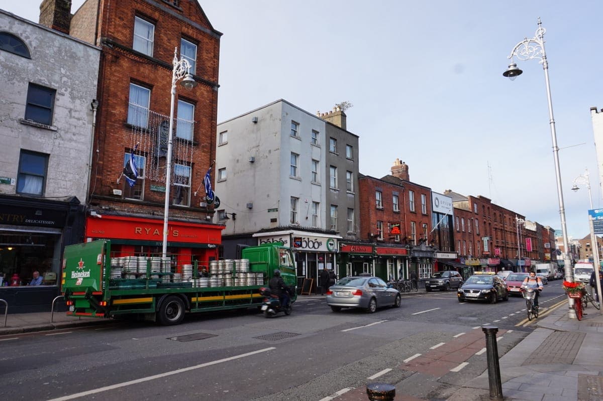 Bunte Pubs und Restaurants säumen die Camden Street in Dublin, mit einem grünen Heineken-Truck, Radfahrern und Fußgängern an einem hellen Nachmittag.