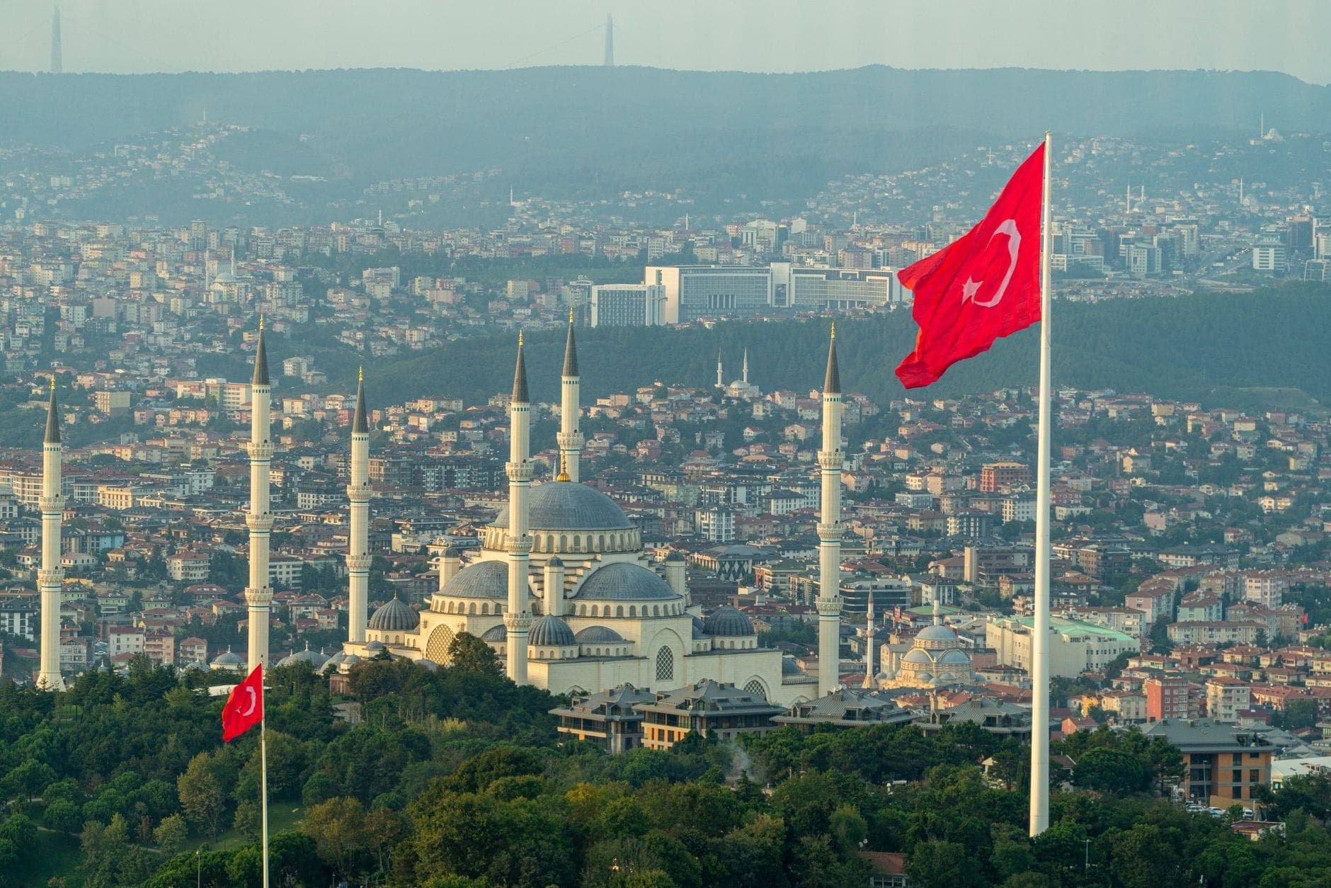 Weiter Blick über den Çamlıca-Hügel mit der großen Moschee, türkischen Flaggen und dem weitläufigen Stadtpanorama Istanbuls im sanften Tageslicht – der höchste Aussichtspunkt der Stadt.