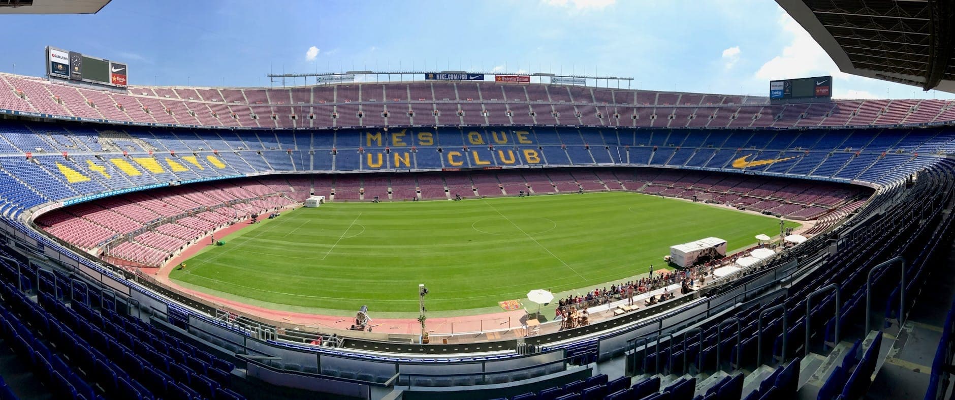 Toàn cảnh sân Camp Nou nhìn từ khán đài, không có khán giả, bầu trời trong xanh, hiện rõ mặt sân và hàng ghế mang dòng chữ MES QUE UN CLUB.