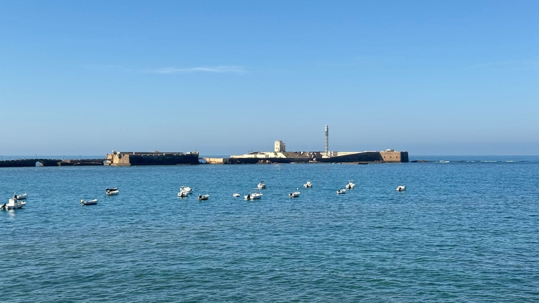 Toàn cảnh pháo đài Castillo de San Sebastián nhìn từ phía Đại Tây Dương xanh, vài chiếc thuyền nhỏ trôi phía trước dưới bầu trời quang đãng.