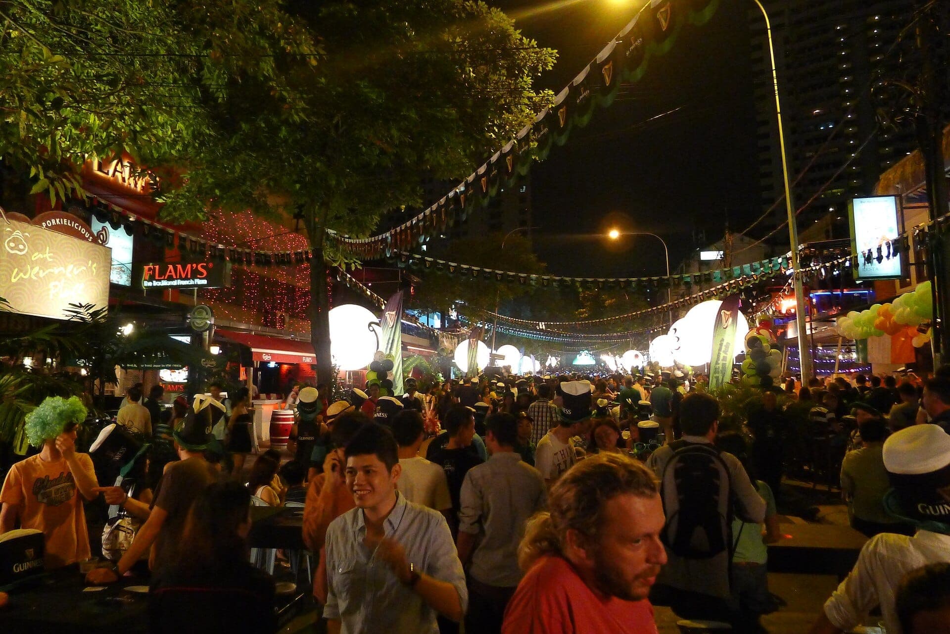 Đám đông tụ tập vào ban đêm trên Changkat Bukit Bintang dưới những ánh đèn lễ hội, xung quanh là các quán bar sôi động, cây xanh và trang trí đường phố nhộn nhịp.