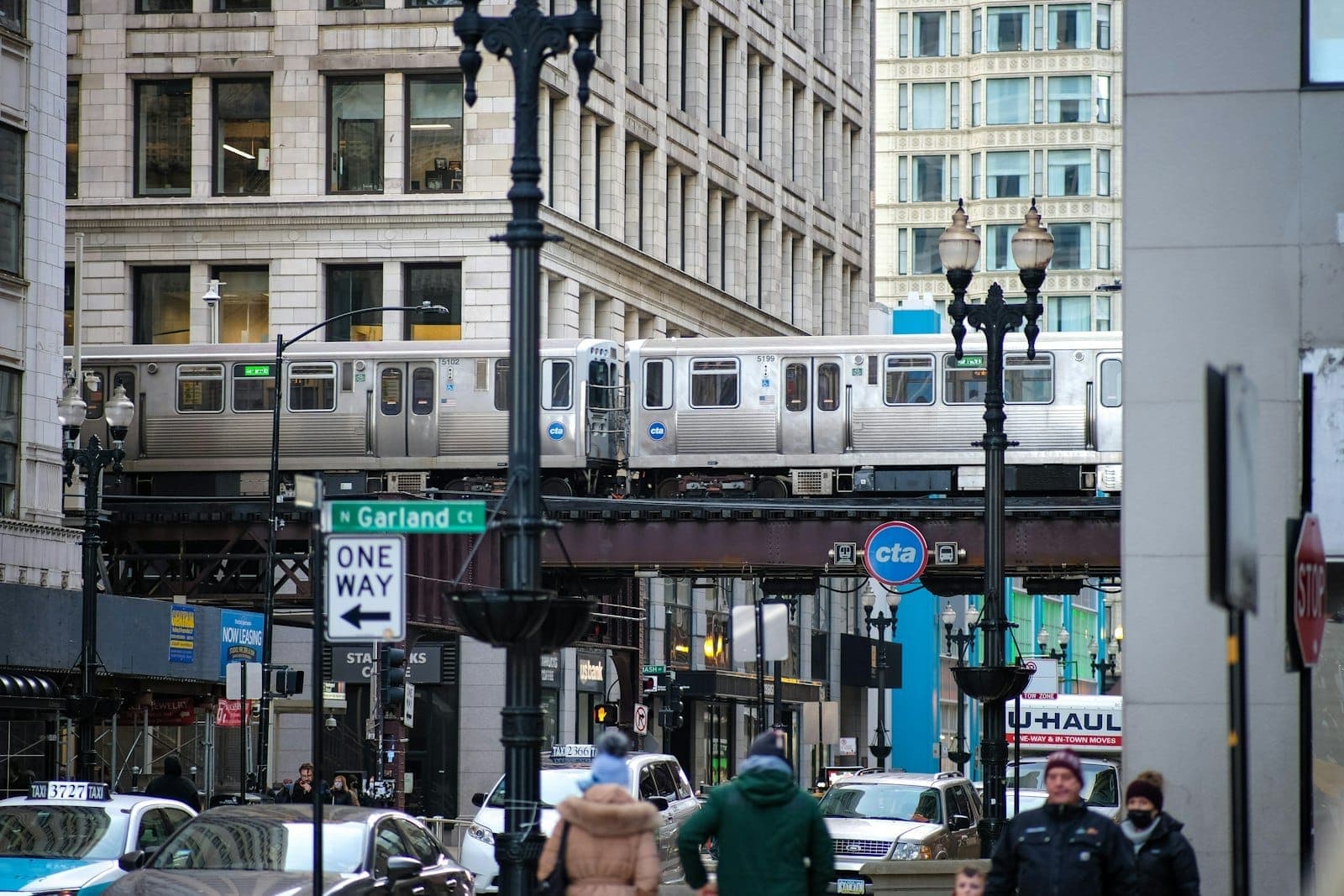 CTA 'L'-Zug in Chicago, der im Stadtzentrum über die Straße fährt, mit sichtbarem CTA-Schild, Stadtstraße und Menschen darunter an einem klaren Tag.