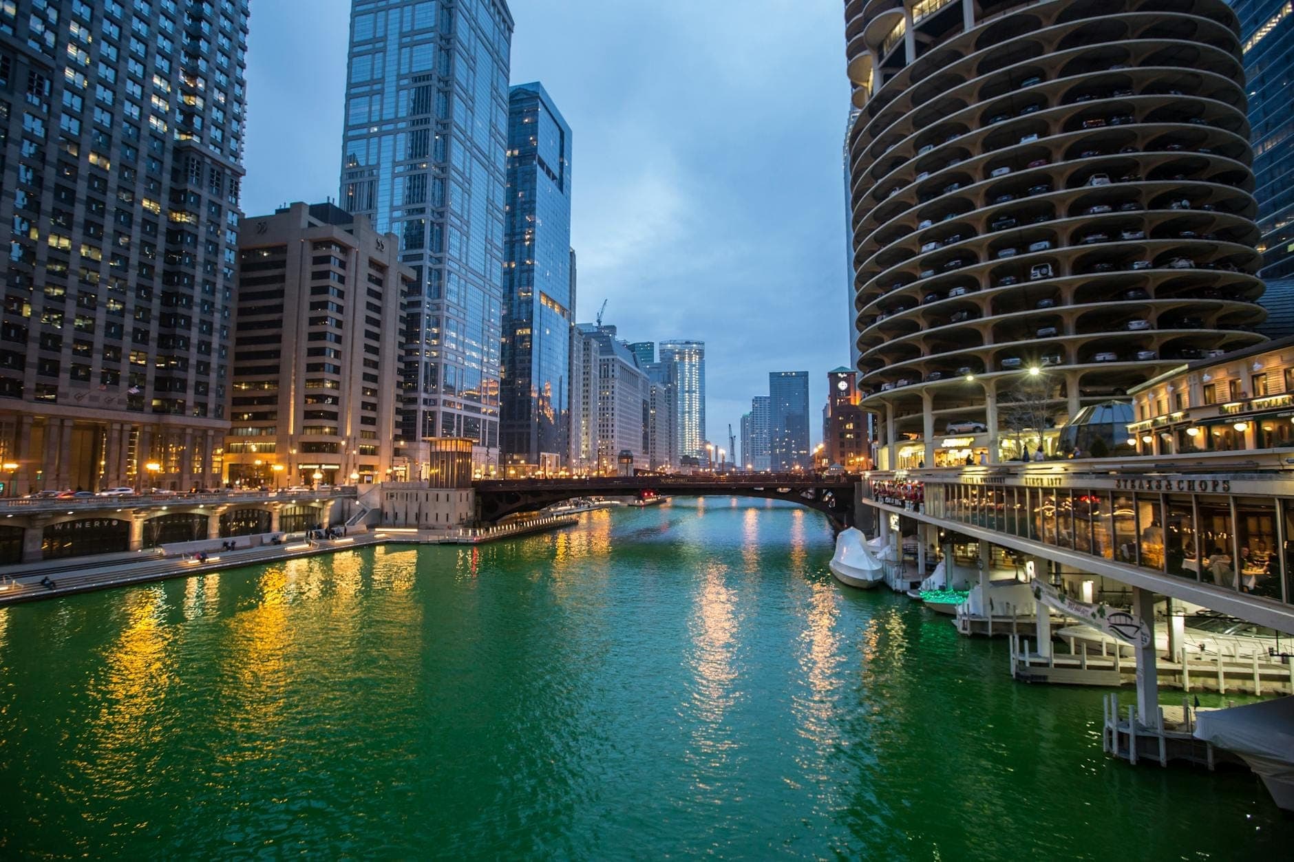 Blick auf den Chicago River, der zum St. Patrick's Day leuchtend grün gefärbt ist, umgeben von Stadtgebäuden und Brücken in der Abenddämmerung.