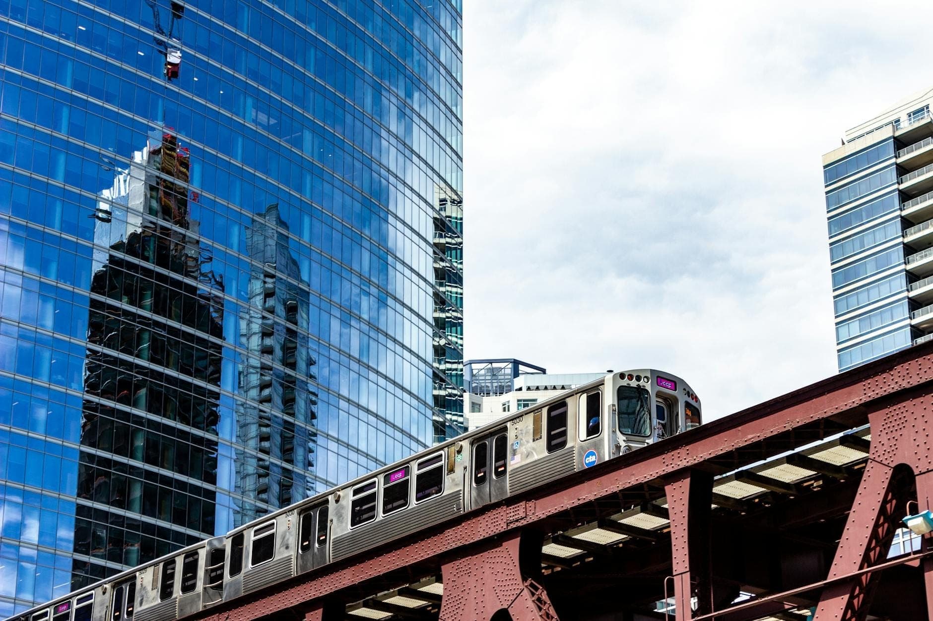 Chicagos Hochbahn 'L' fährt durch die Innenstadt mit gläsernen Wolkenkratzern im Hintergrund an einem klaren Tag