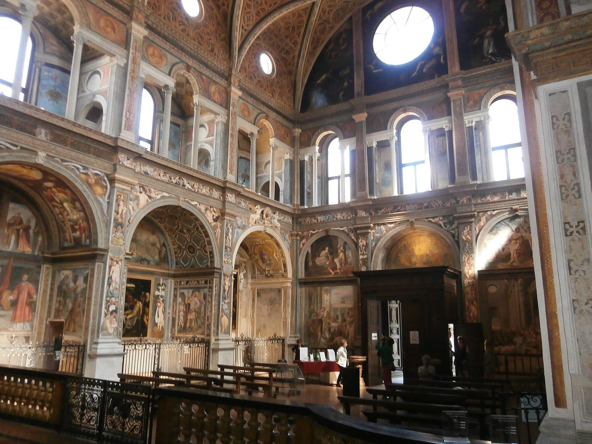 Interior view of Chiesa di San Maurizio al Monastero Maggiore in Milan, featuring Renaissance frescoes, ornate arches, and tall arched windows.