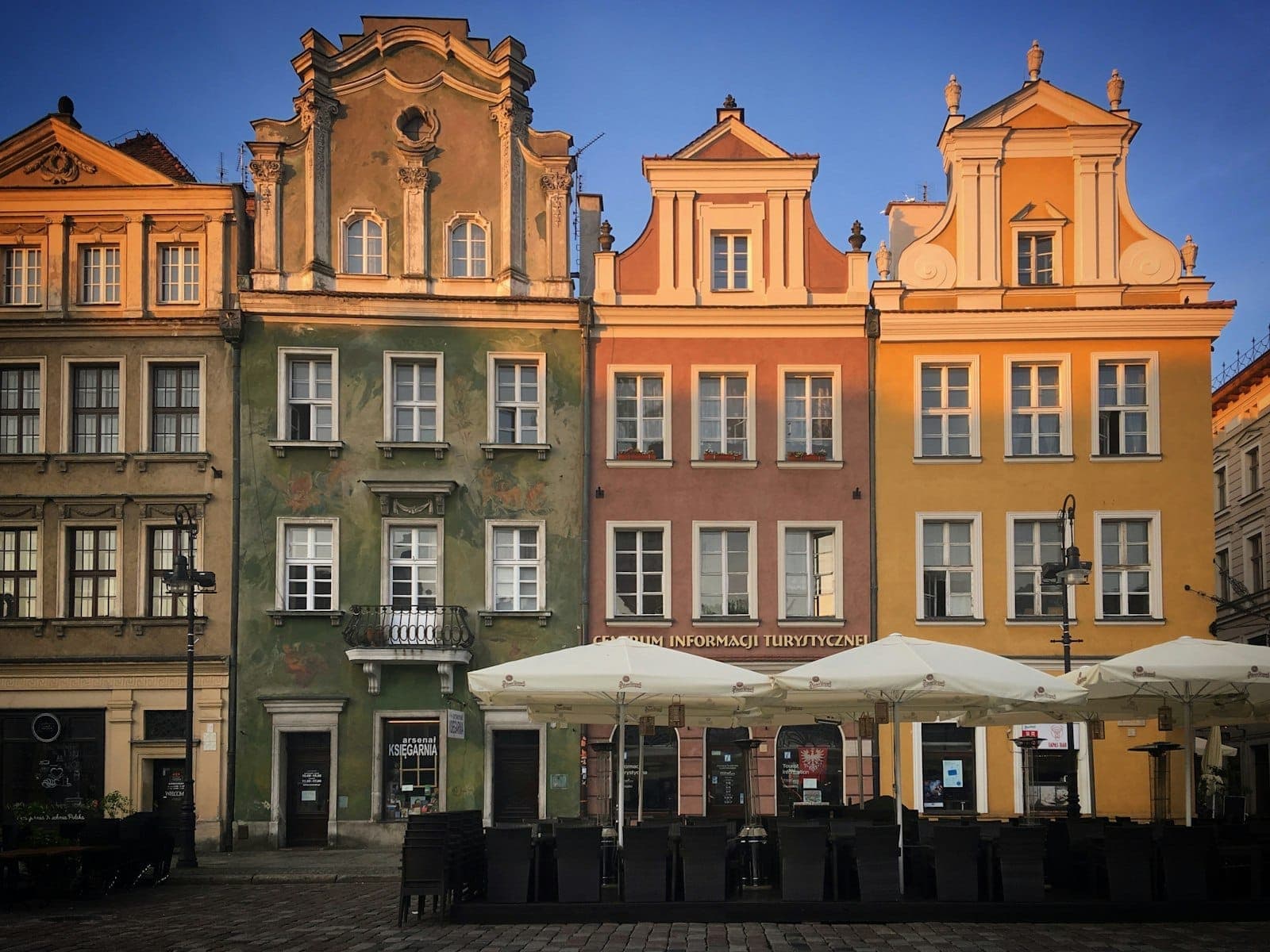 Colorate case storiche con facciate ornate nella piazza della Città Vecchia di Varsavia, luce del pomeriggio, tavolini di caffè con ombrelloni in primo piano.