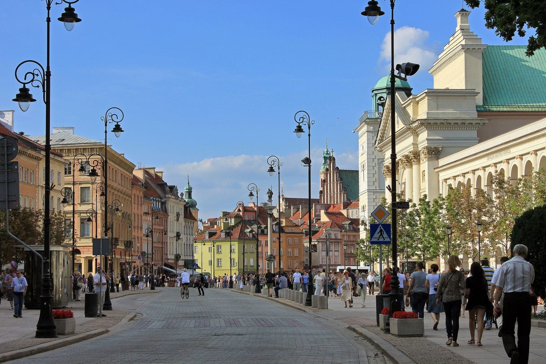 Vista ampia di Krakowskie Przedmieście a Varsavia, fiancheggiata da edifici storici e animata da pedoni in una giornata di sole.