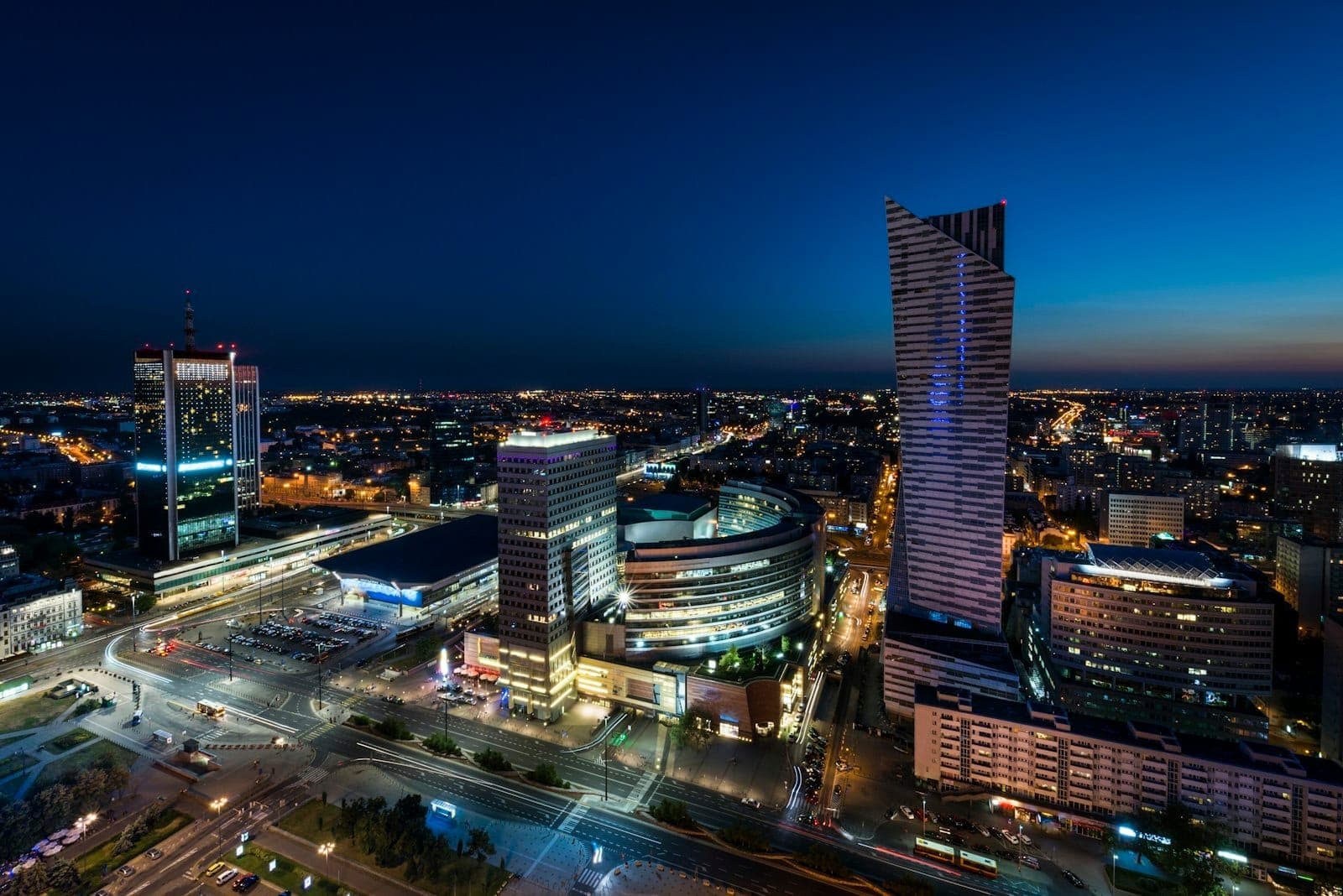Warschaus Stadtzentrum am Abend: beleuchtete Hochhäuser, belebte Straßen und ein tiefblauer Himmel über dem Herzen des Bezirks Śródmieście.