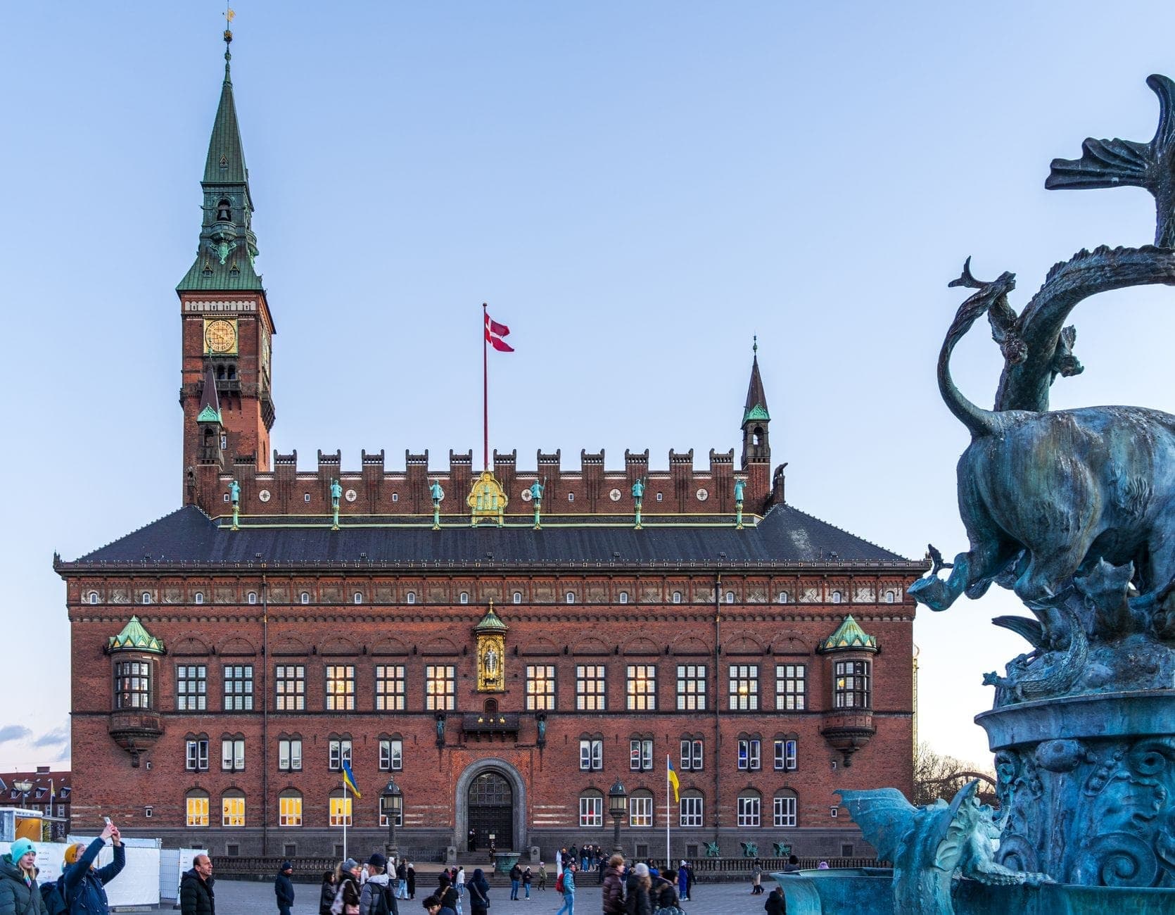 Das Kopenhagener Rathaus vom Rådhuspladsen aus gesehen, mit Passanten auf dem Platz und einem Drachenbrunnen im Vordergrund.